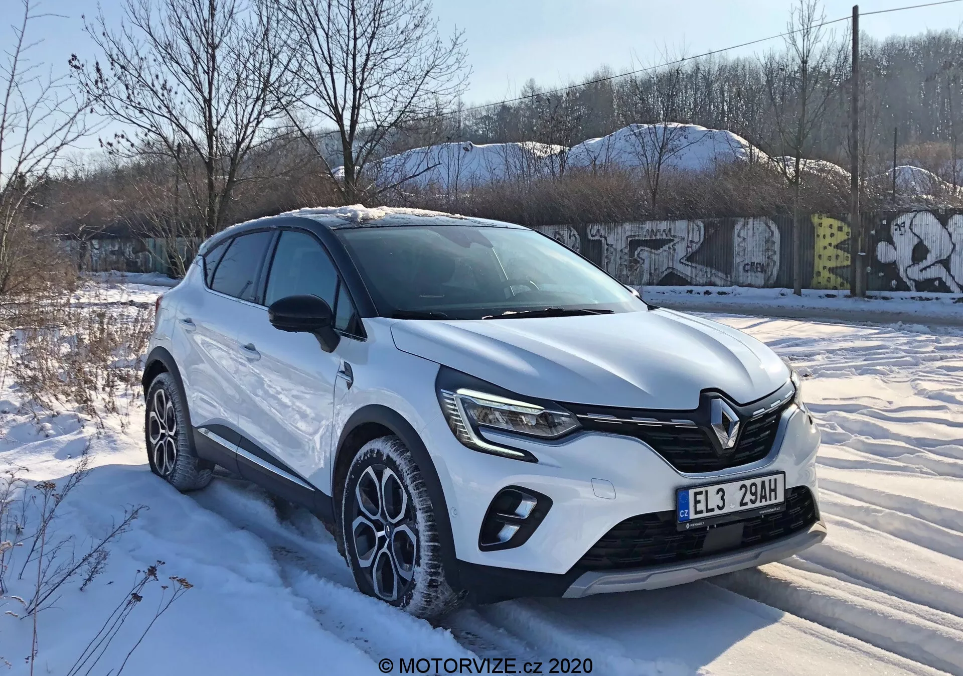 Renault Captur 2020 en vista de tres cuartos frontal mostrando un diseño moderno de crossover con una parrilla frontal distintiva, faros LED afilados, molduras de carrocería, grandes llantas de aleación multifuncionales y un color de carrocería blanco bajo condiciones invernales nevadas en un entorno urbano.