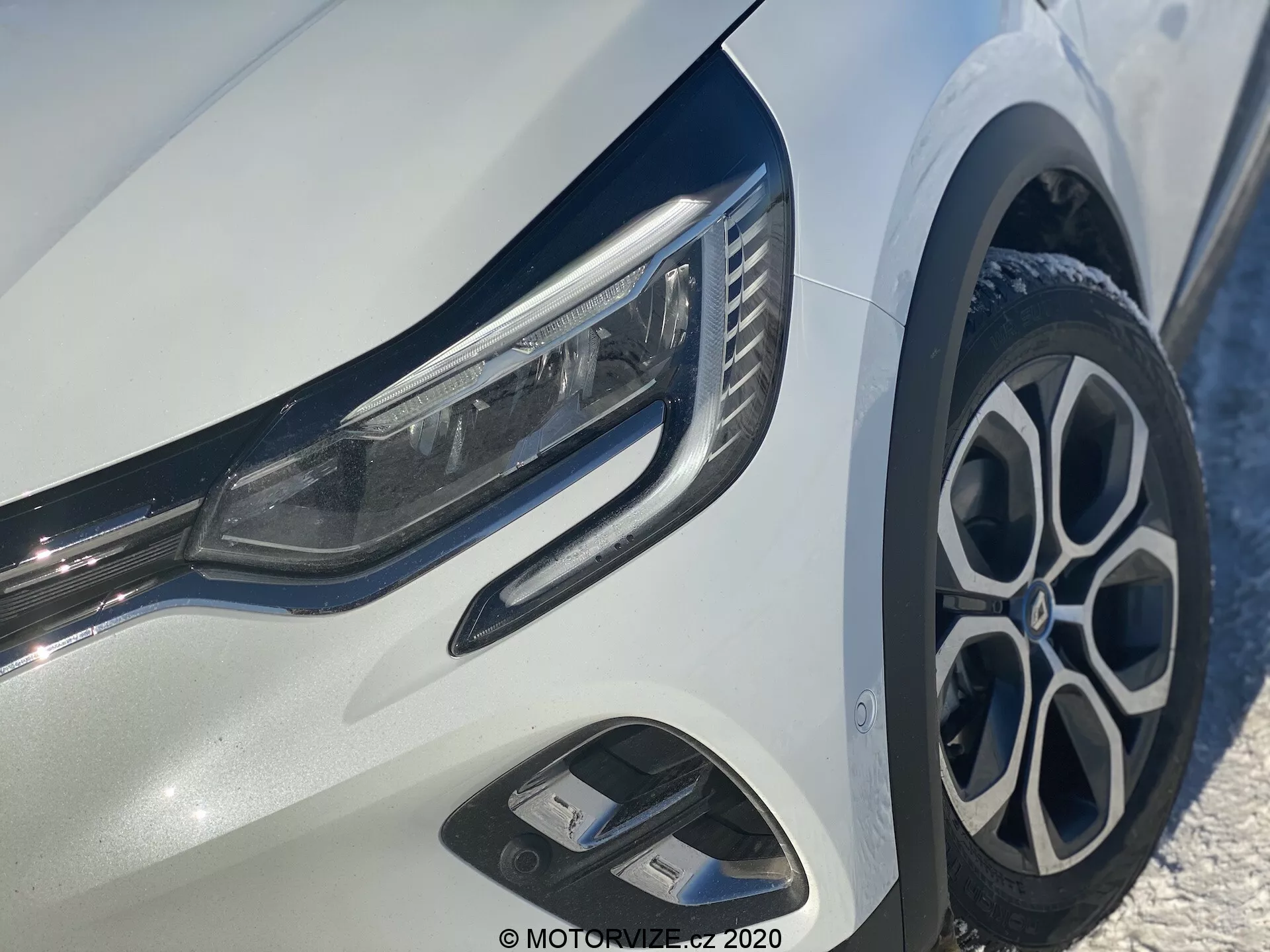 Vista de cerca del Renault Captur 2020 enfocada en el cuarto delantero izquierdo, mostrando faros LED elegantes, llantas de aleación multirradio elegantes, parachoques delantero dinámico con entradas de aire y acabados cromados y brillantes en un cuerpo blanco brillante.