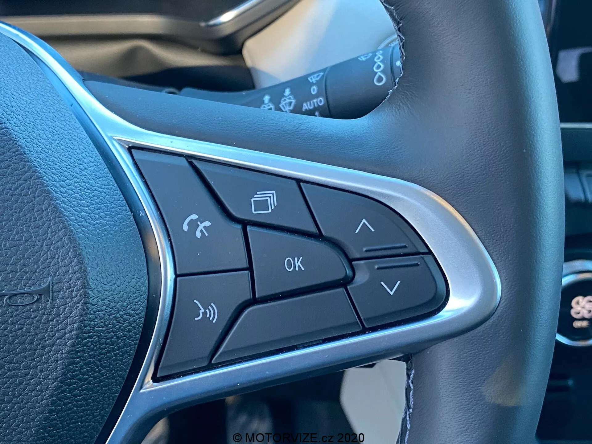 Vista de primer plano de los botones de control en el radio del volante del Renault Captur 2020. Incluye activación de comandos de voz, gestión de llamadas telefónicas, controles de volumen, botón de OK y flechas de navegación de menú. El diseño elegante incluye un borde plateado que destaca los botones, enfatizando la operación manos libres y la comodidad.