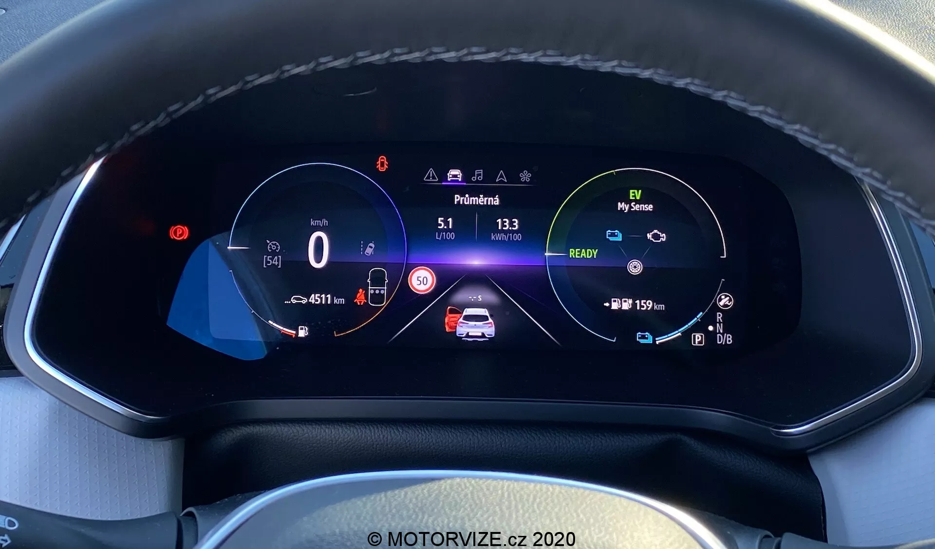 Vista en primer plano del cuadro de instrumentos digital del moderno Renault Captur 2020 desde la perspectiva del conductor. La pantalla completamente digital y de alta resolución a color, situada en un tablero texturizado con costuras visibles, muestra un velocímetro en 0 km/h con un límite de velocidad de 50 km/h, un gráfico central animado del coche con alertas de seguridad e indicadores de batería, un tacómetro con icono de modo ecológico 'My Sense', odómetro, temperatura exterior, indicador de marcha en 'Park' e iconos para asistencia de mantenimiento de carril, luces altas automáticas y control de crucero adaptativo, todo en un diseño bien organizado que resalta la avanzada tecnología y diseño interior del automóvil.