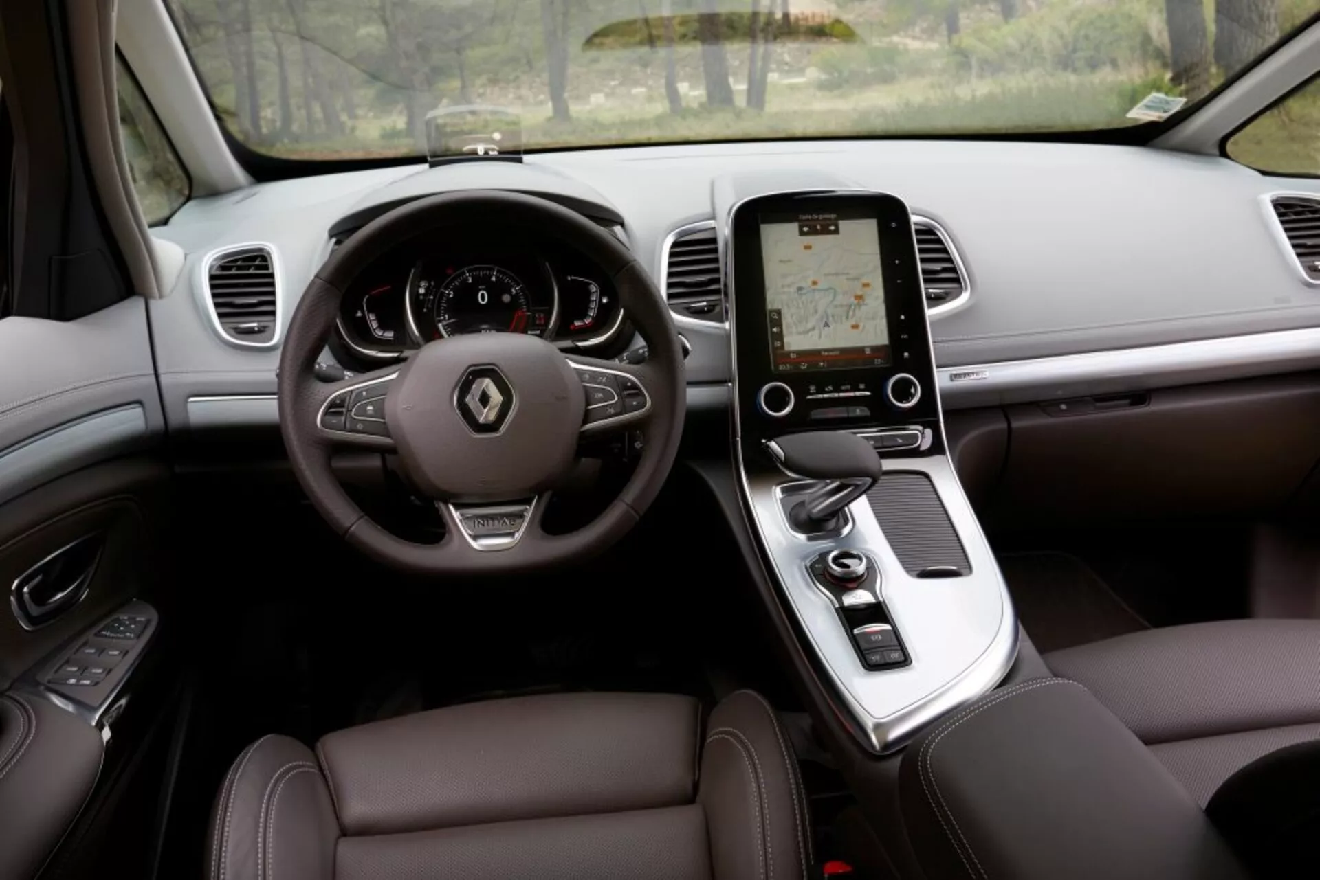Vista interior del Renault Espace 2015 desde el asiento del conductor mostrando un lujoso diseño, con volante de tres radios con botones de control, cuadro de instrumentos digital, consola central con pantalla táctil vertical para el sistema de infoentretenimiento, palanca de cambios automática, asientos tapizados en cuero con ajuste electrónico y rejillas de ventilación del tablero para el control del clima