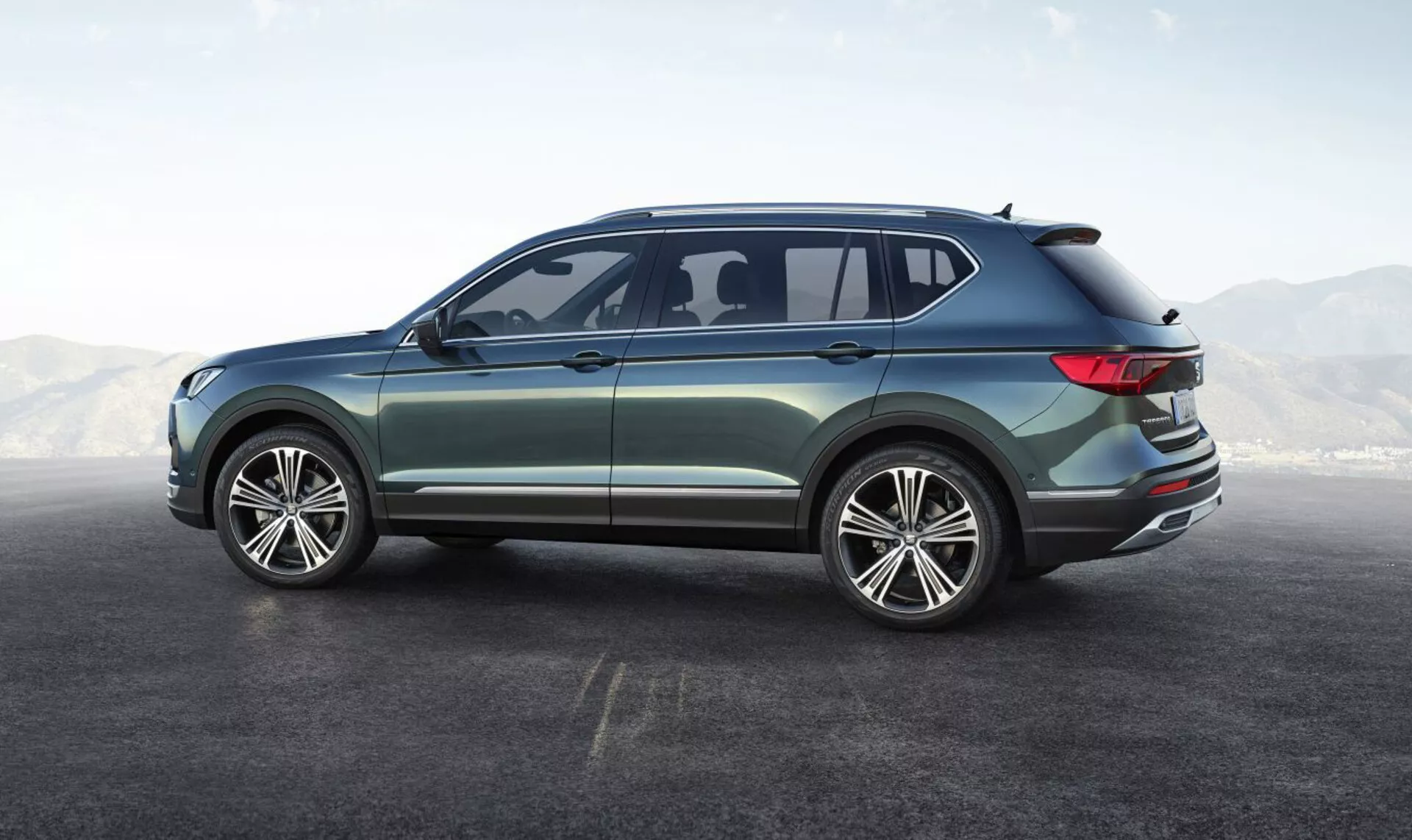 SUV Seat Tarraco 2019 mostrando su ángulo trasero lateral, con grandes ruedas de aleación de múltiples radios, diseño de cuatro puertas, ventanas laterales elegantes con una pequeña ventana trasera aerodinámica, línea de techo suavemente inclinada con spoiler integrado, luces traseras LED envolventes, pintura metálica con ribete exterior cromado, destacando su diseño moderno y versátil