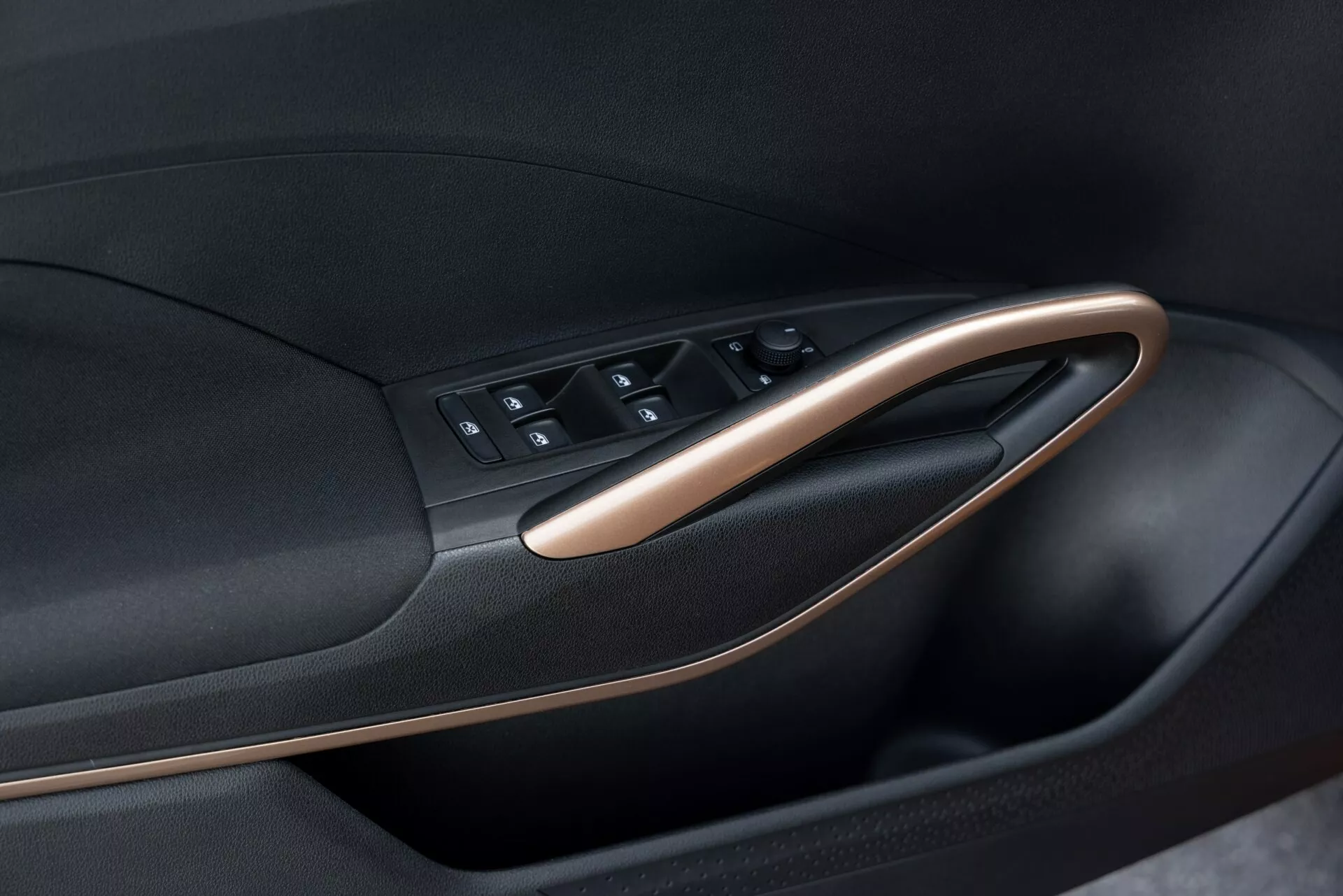 Vista de cerca del panel interior de la puerta del Skoda Fabia 2021, destacando el módulo de control de la puerta. La imagen, tomada desde un ángulo oblicuo, resalta la disposición de los botones y el recorte de la puerta. El módulo de control de la puerta incluye botones para los controles de las ventanas, los bloqueos de las puertas y posiblemente los ajustes de los espejos. El panel presenta un diseño bicolor con material negro acentuado por molduras metálicas o de madera, enfatizando el diseño moderno y ergonómico del coche.