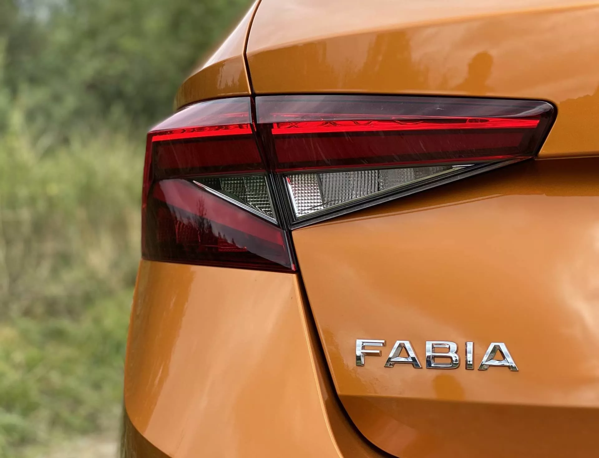 Imagen en primer plano de la esquina trasera de un Skoda Fabia 2021 que destaca el diseño angular y afilado del conjunto de luces traseras LED y la distintiva marca 'FABIA' en la carrocería de tono metálico naranja brillante. Las curvas suaves y los ligeros abultamientos alrededor de las luces traseras realzan la estética moderna, capturada desde un ángulo ligeramente elevado y con poca profundidad de campo.
