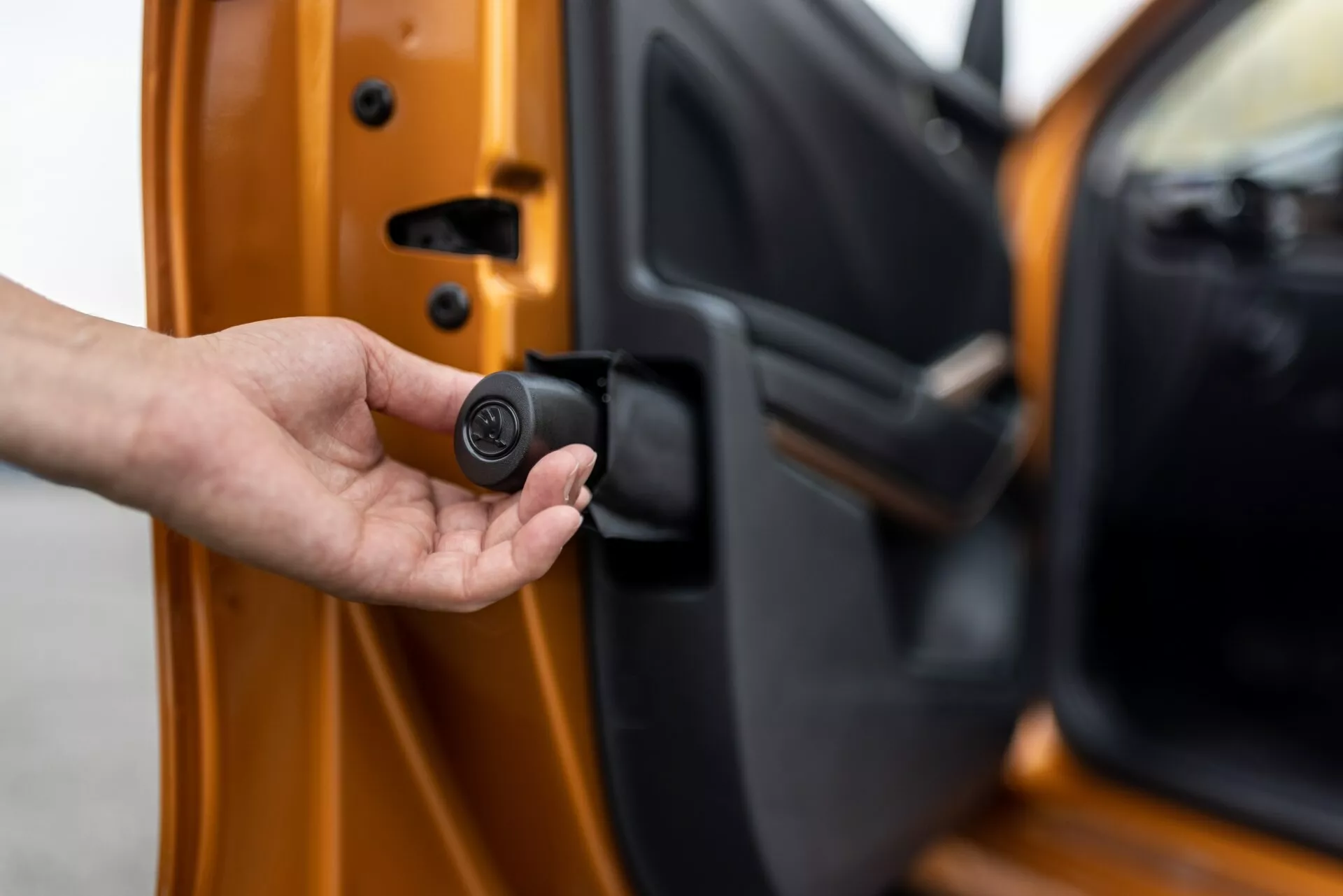 Primer plano de la puerta del conductor del Skoda Fabia 2021, ligeramente entreabierta, vista desde el exterior con el borde interior visible. Una mano sostiene un llavero negro y circular compacto que indica un sistema de entrada sin llave o de seguridad del automóvil. El coche es de color naranja brillante con un acabado metálico, mostrando mecanismos de bloqueo avanzados y características de seguridad personalizadas.