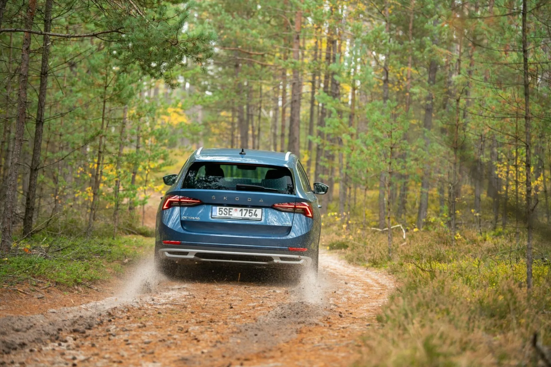 Limusina Skoda Octavia 2017 en azul, mostrando luces traseras LED, limpiaparabrisas trasero y doble escape en un sendero forestal con desplazamiento dinámico de tierra indicando capacidades de tracción total