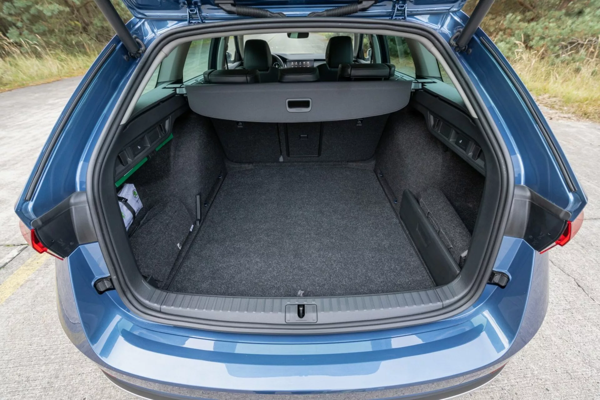 Vista trasera de un Skoda Octavia Limousine 2017 destacando su amplio y limpio espacio de maletero con portón trasero abierto, cubierta de carga retráctil y asientos traseros visibles en configuración dividida 60/40 para mayor capacidad de carga, junto a un pequeño paraguas y un objeto verde, bajo luz ambiental.