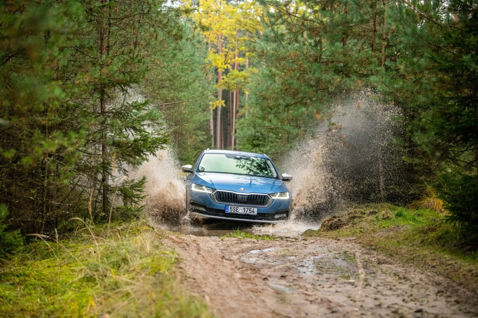 Limusina Skoda Octavia de 2017 atravesando un charco de barro en una zona boscosa, destacando su dinámica creación de salpicaduras, parrilla frontal, faros y capó con una vista parcial del techo desde un ángulo frontal derecho.