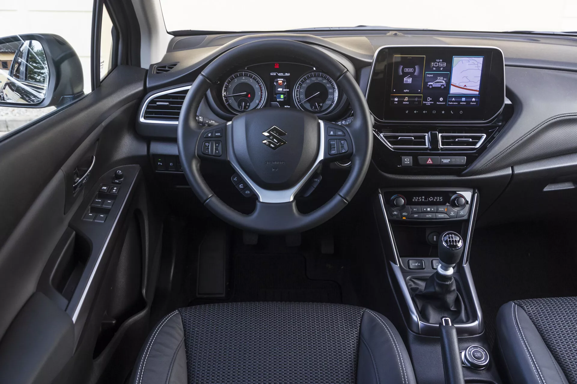 Interior de la cabina frontal del Suzuki S-Cross 2022 mostrando el tablero de instrumentos, volante con controles montados, cuadro de instrumentos digital-analógico, sistema de infoentretenimiento táctil, diales de control climático, palanca de cambios de cuero, selector de modo de conducción, freno de estacionamiento electrónico y panel de la puerta con botones de control de energía