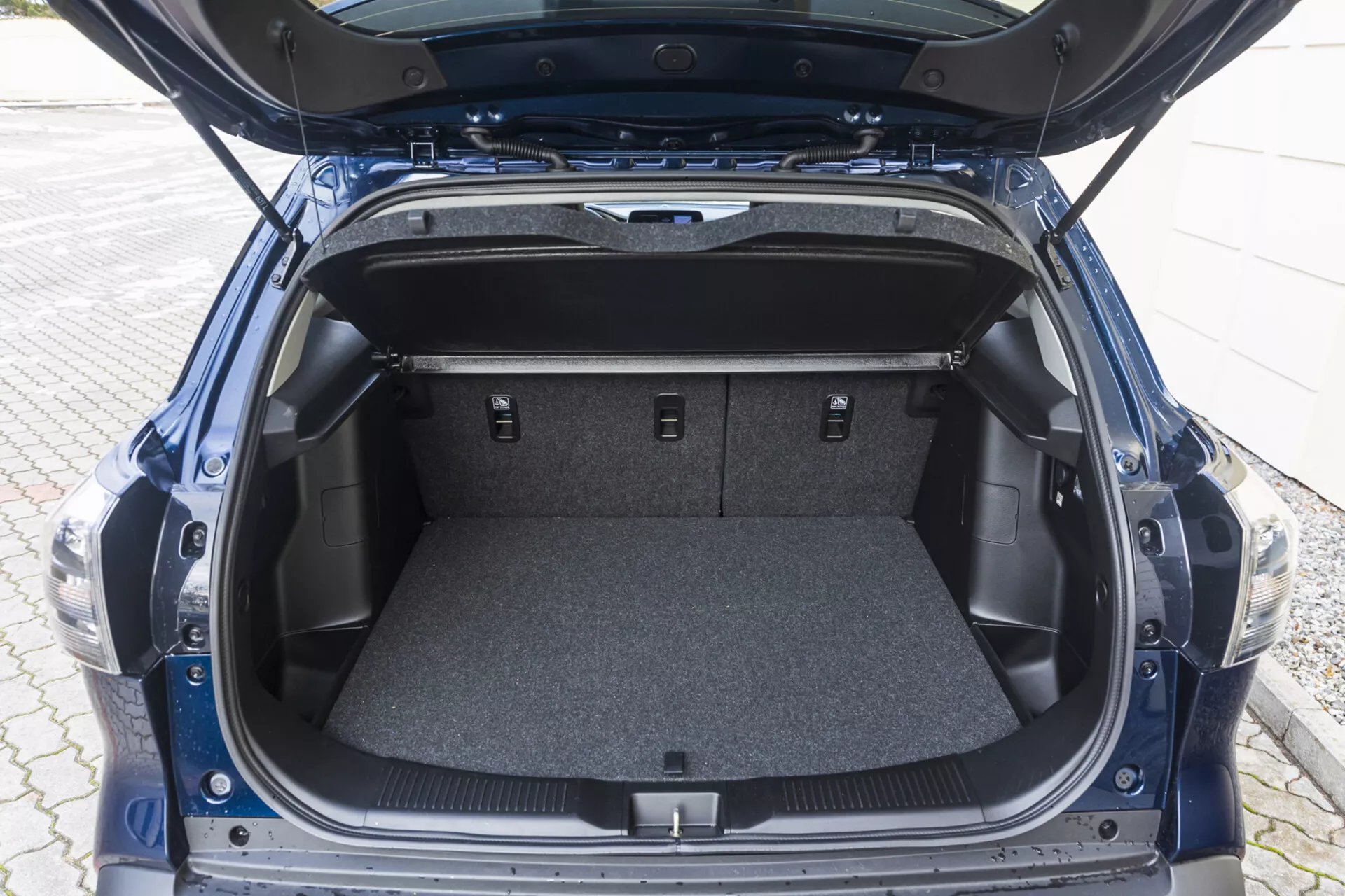 Vista del espacio del maletero trasero de Suzuki S-Cross 2022 con la tapa abierta mostrando un área alfombrada vacía, compartimentos laterales y asientos traseros abatidos