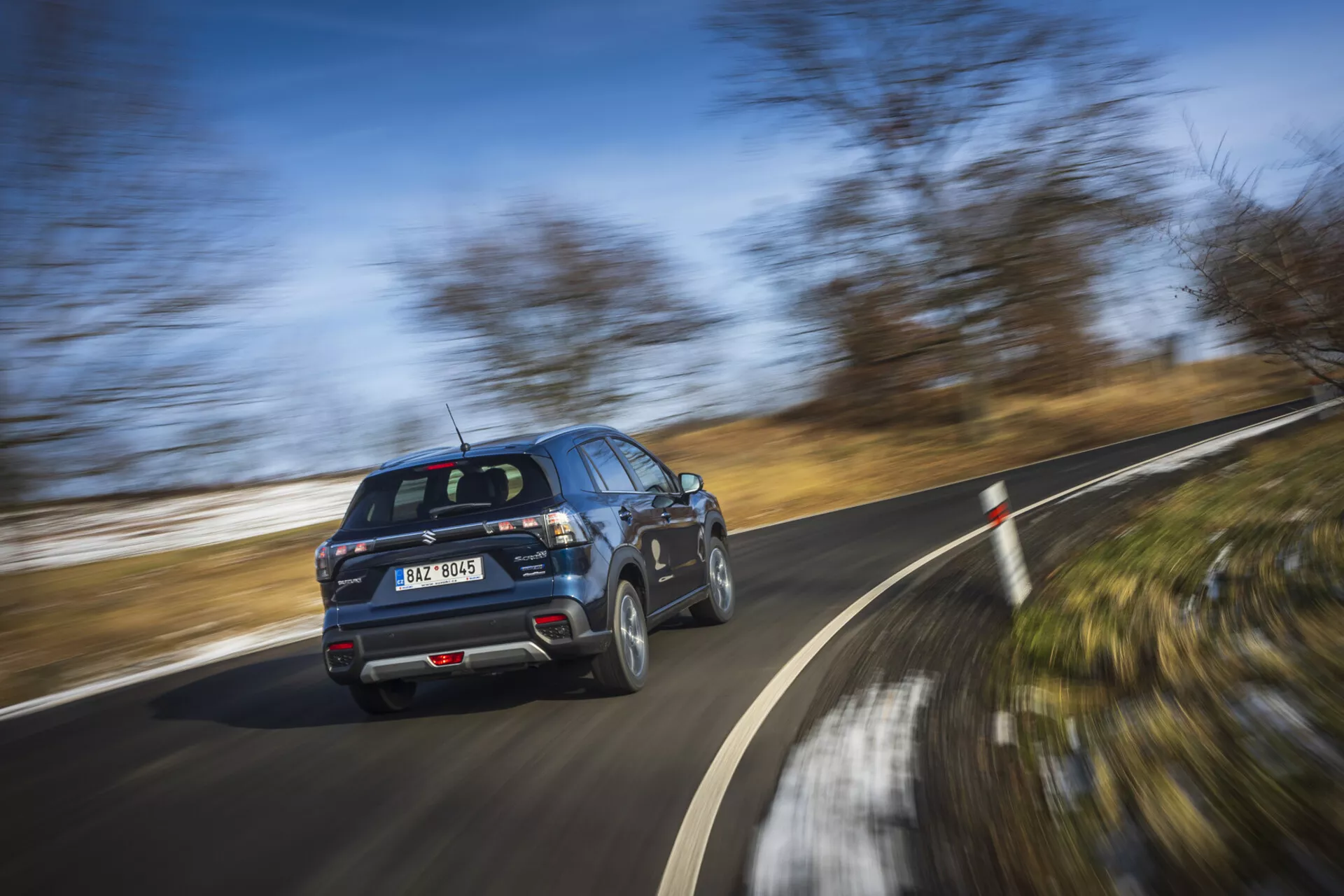 SUV moderno Suzuki S-Cross 2022 en movimiento, mostrando perfil desde una vista trasera de tres cuartos con ruedas girando en un día claro