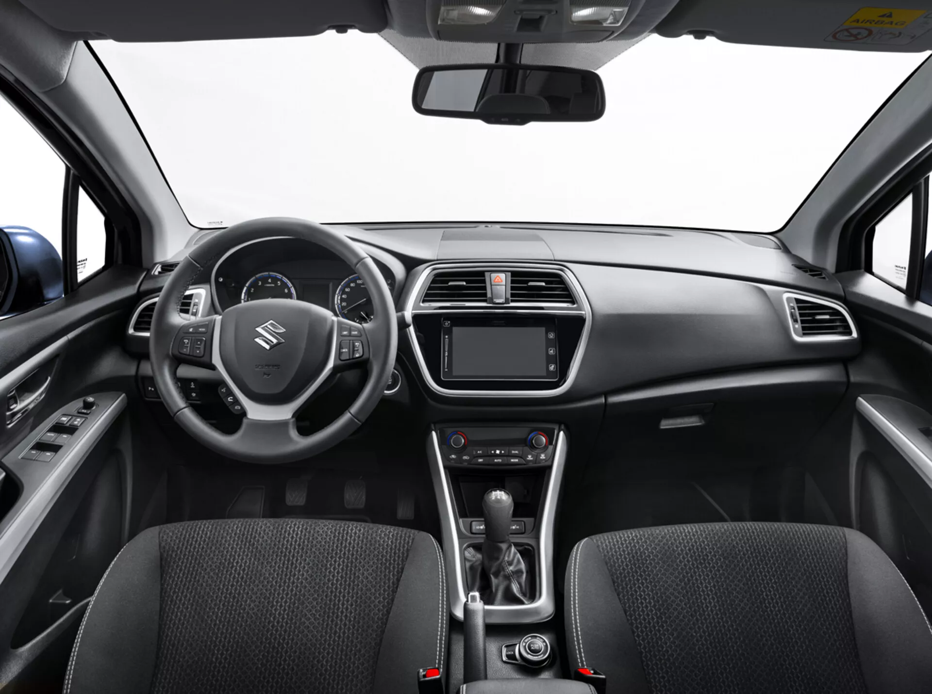Vista interior del Suzuki S-Cross 2022 desde el asiento trasero mostrando el tablero de instrumentos, volante con controles, panel de instrumentos digital, sistema de infotenimiento, controles de clima, palanca de cambios automática, y asientos delanteros detallados con textura de tela