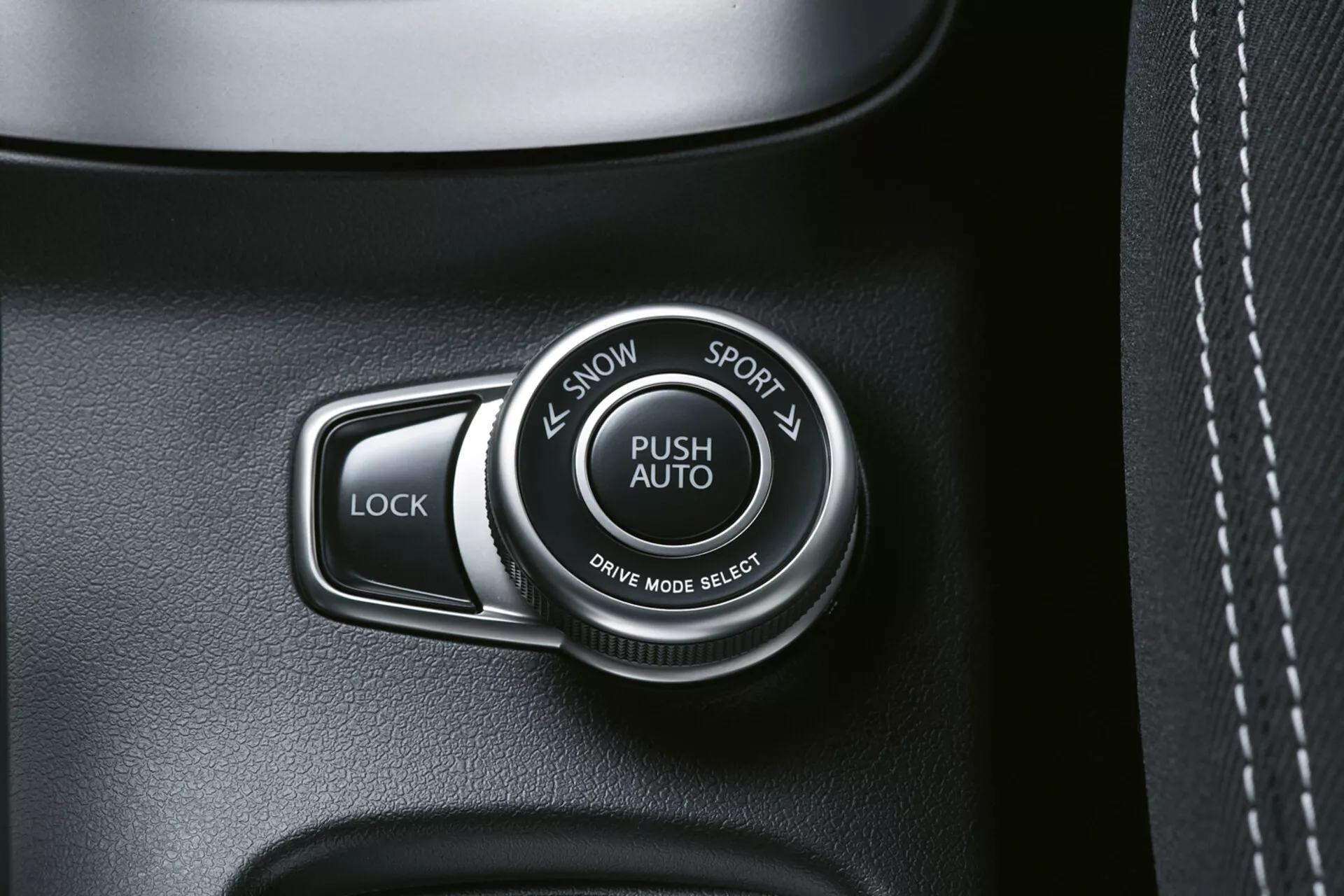 Vista detallada del interior del Suzuki S-Cross 2022 mostrando el selector de modo de conducción etiquetado como 'PUSH AUTO' con opciones 'SNOW' y 'SPORT', junto a un botón 'LOCK', en un panel oscuro de alta calidad, posiblemente con textura de cuero y costuras visibles.