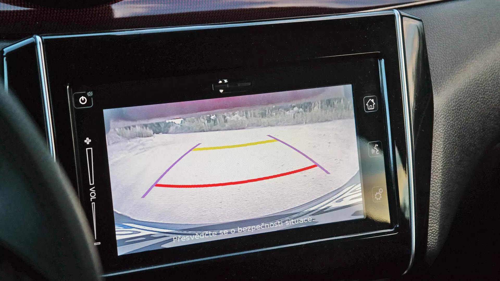 Vista de cerca de la pantalla de la cámara trasera en el sistema de infoentretenimiento del Suzuki Swift Sport 2017, mostrando guías de alineación y un entorno nevado, con un mensaje de advertencia aconsejando revisar los alrededores.