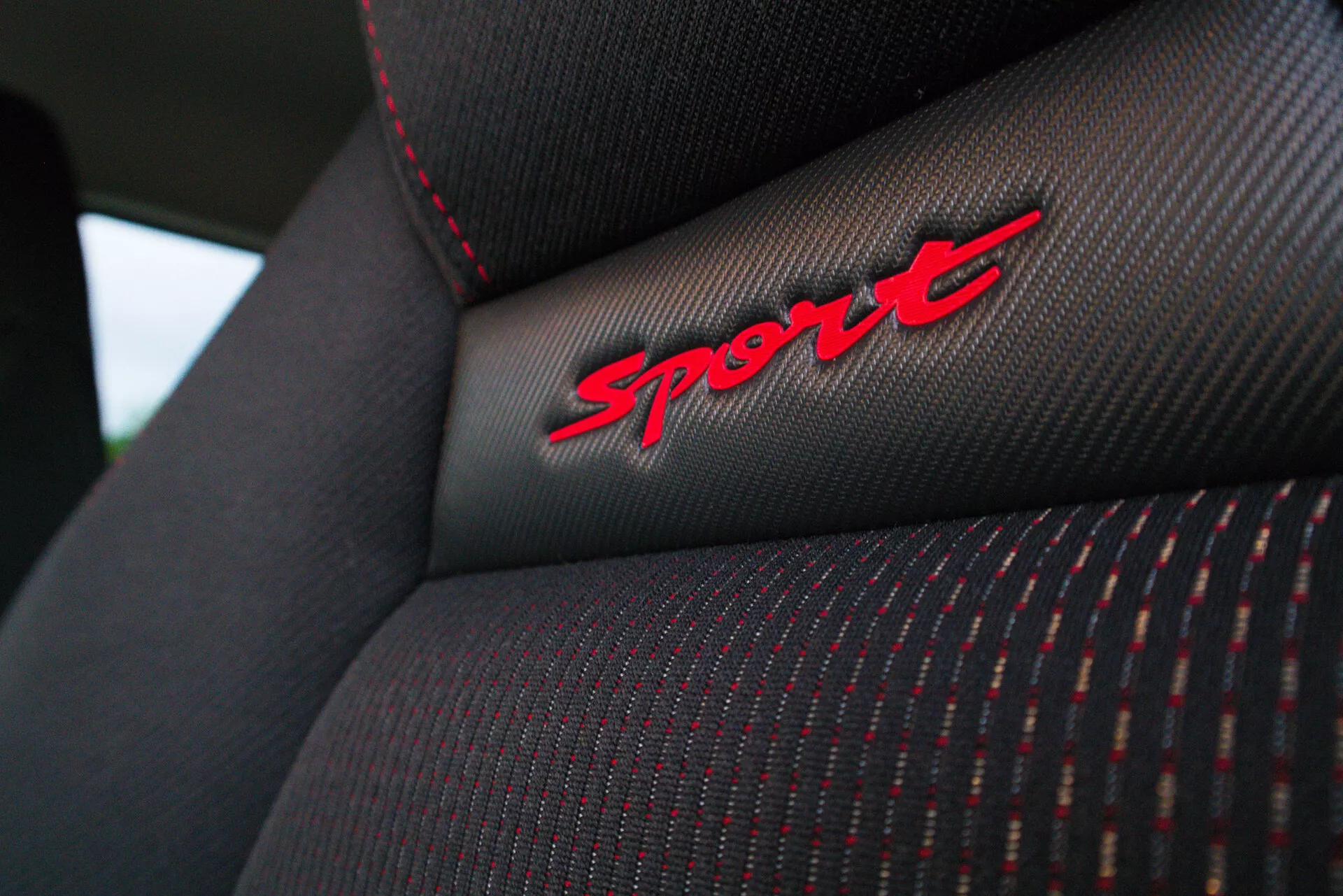 Vista de cerca del respaldo del asiento del Suzuki Swift Sport 2017, mostrando la textura detallada de la tela, costuras rojas y el bordado 'Sport' en una tela negra, destacando el nivel deportivo del vehículo.