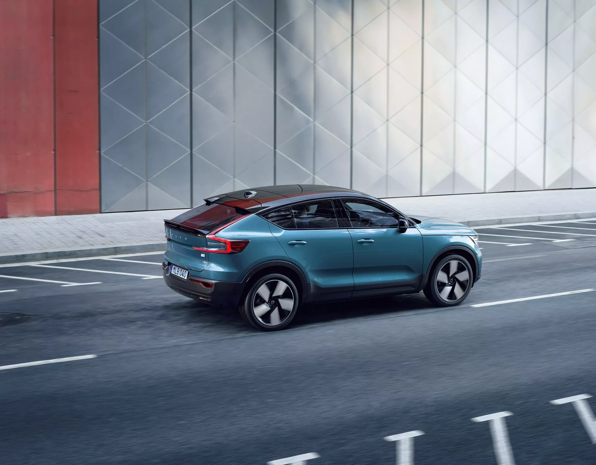 Vista dinámica trasera de tres cuartos del Volvo C40 2021, mostrando su diseño elegante, elementos aerodinámicos, luces traseras modernas, ruedas personalizadas y techo panorámico, mientras se mueve por una carretera urbana.