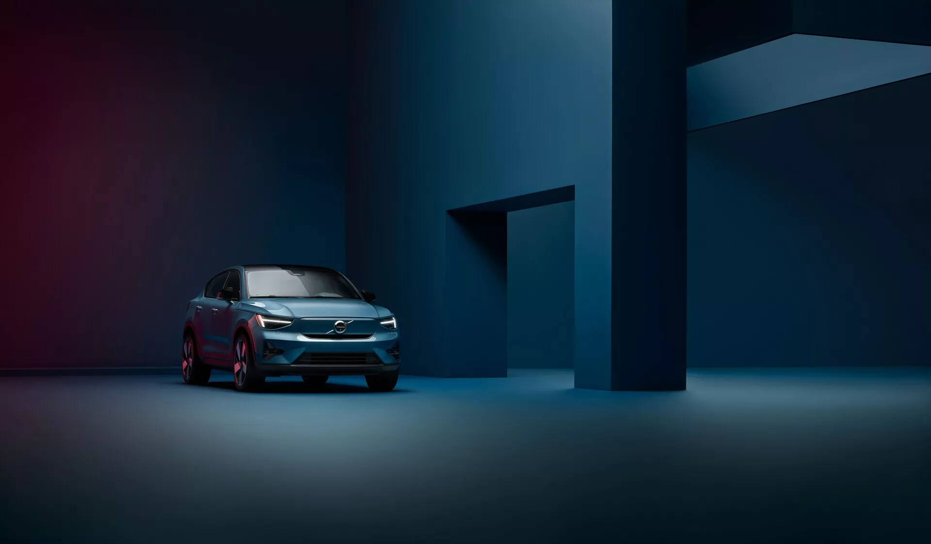 Una fotografía profesional de un Volvo C40 2021 (1ª generación) desde una vista de tres cuartos delantera que destaca la rejilla moderna, los faros LED y el perfil lateral elegante en un entorno de estudio tenuemente iluminado y atmosférico.