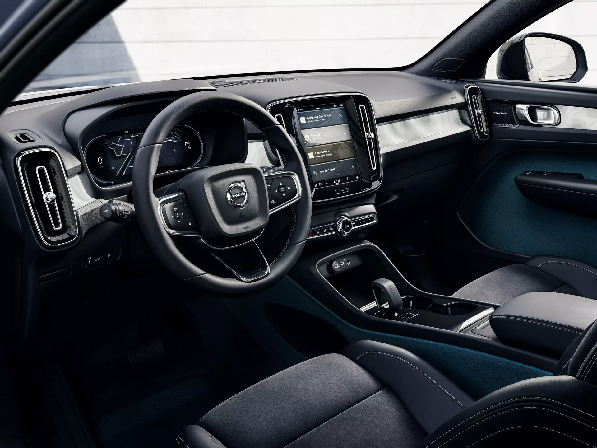 Imagen del interior de un Volvo C40 2021 (1ª generación) desde una perspectiva exterior, mostrando la cabina del conductor con el volante, el panel de instrumentos digital, la consola central con el sistema de infoentretenimiento táctil, los controles de clima, asientos ergonómicos de tela oscura, botones de control de puertas y un esquema de color de dos tonos con elementos de diseño modernos y funcionales.