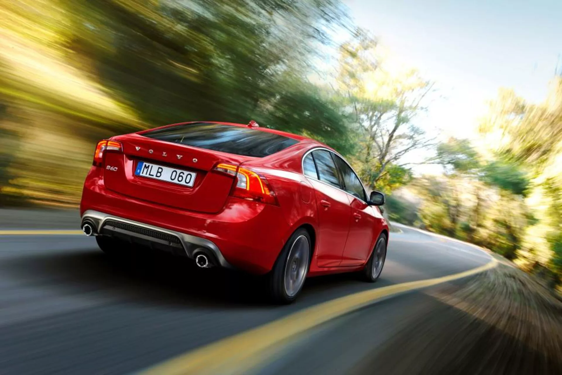 Vista dinámica trasera lateral de un Volvo S60-V60 2004 rojo en movimiento, mostrando luces traseras LED, doble escape, llantas de aleación elegantes y una clara indicación de velocidad a través del efecto de desenfoque de movimiento.