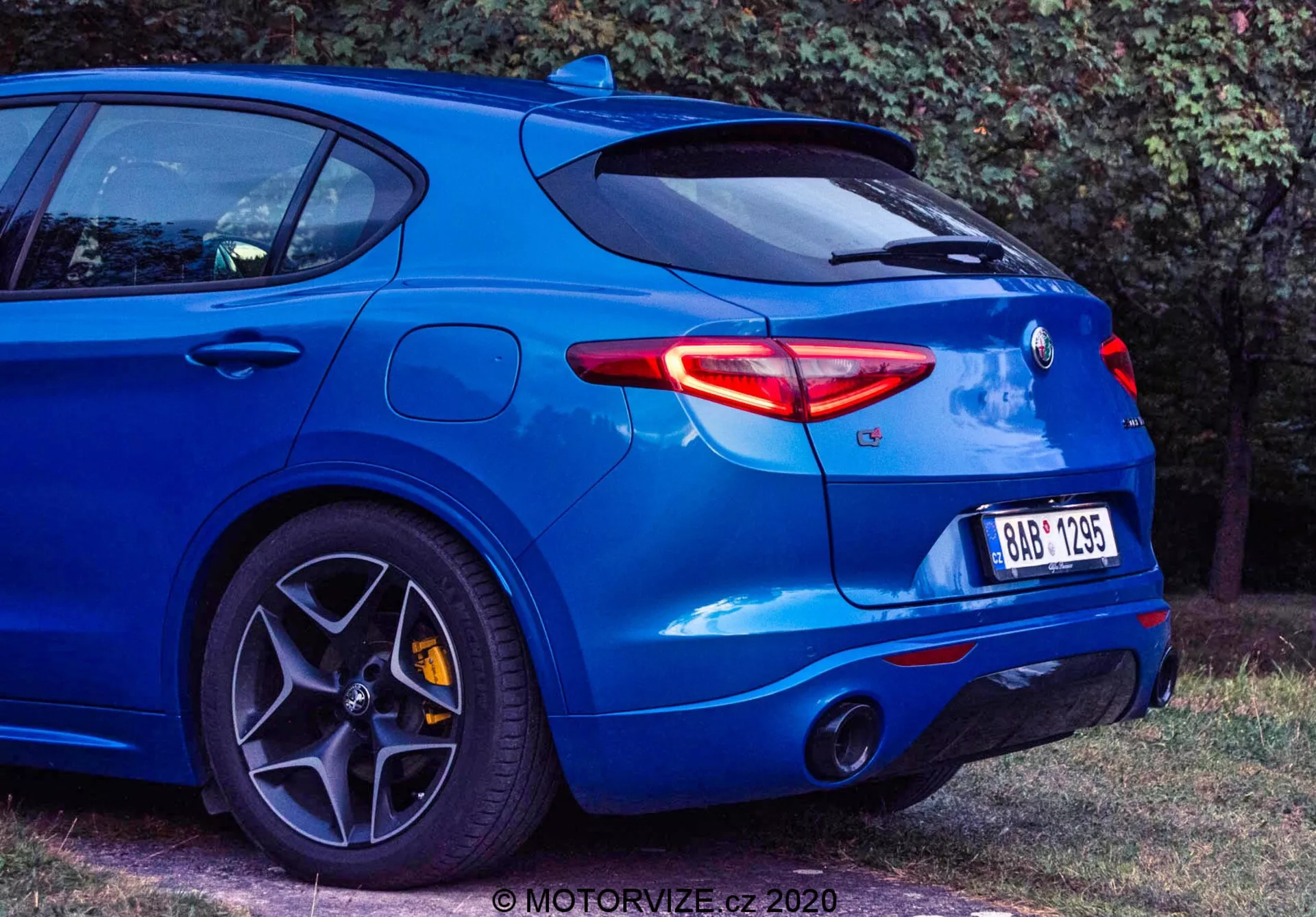 Vista trasera de tres cuartos de un hatchback azul Alfa Romeo Stelvio 2017, capturada desde un ángulo bajo para mostrar sus modernas características de diseño, incluidas las elegantes luces traseras LED, el sistema de escape doble, el distintivo trasero centrado, el spoiler trasero montado en el techo, las grandes llantas de aleación multiradio con frenos de alto rendimiento, neumáticos de perfil bajo y una carrocería musculosa con guardabarros trasero abultado. El vehículo exuda una estética deportiva y orientada al rendimiento. Se puede ver una marca de agua en la esquina inferior derecha.