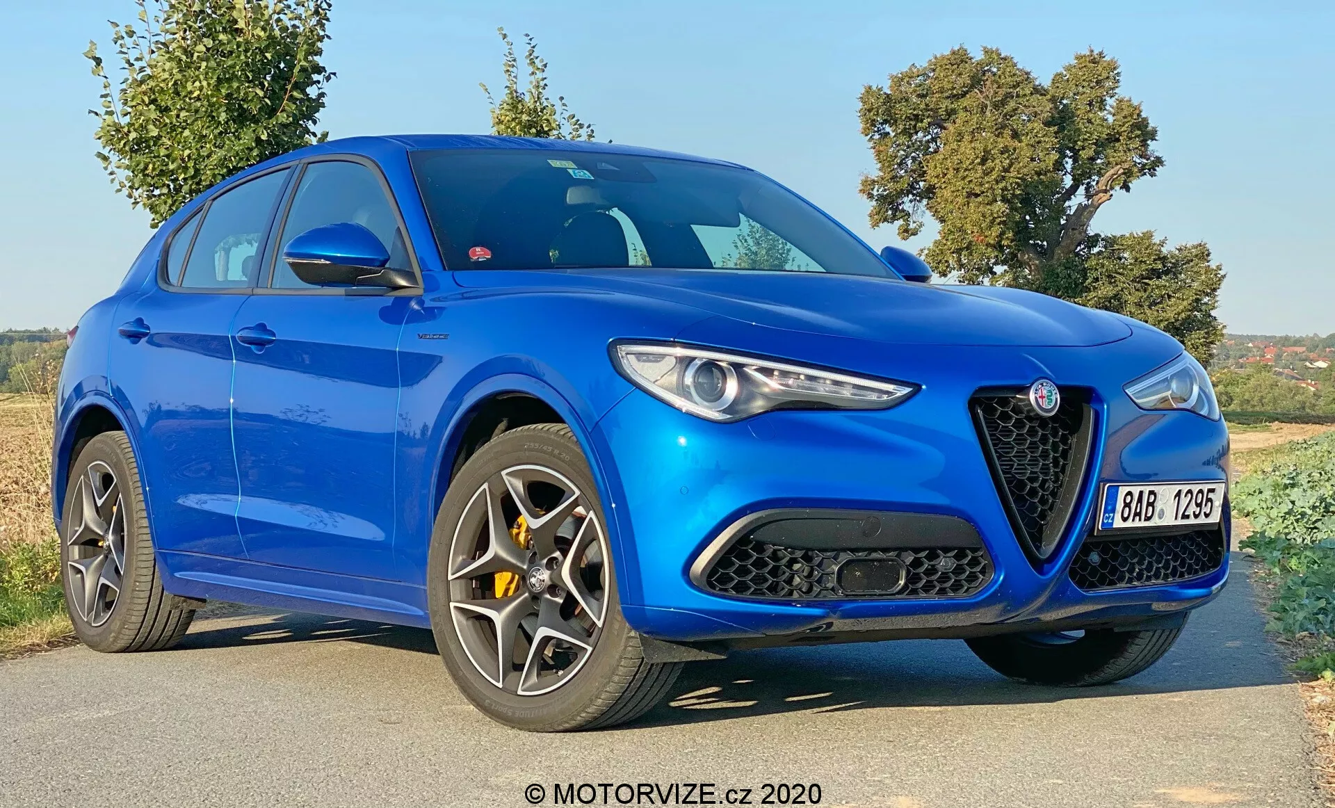 Vista de tres cuartos delanteros del Alfa Romeo Stelvio 2017 en azul brillante, destacando su distintiva parrilla triangular con un logotipo prominente, faros estrechos y elegantes, contornos pronunciados del capó y ruedas de múltiples radios. Esta imagen captura el diseño agresivo y moderno del vehículo con grandes entradas de aire en el parachoques delantero, una silueta deportiva con una línea de techo descendente y líneas esculpidas en la carrocería, sugiriendo una identidad orientada al rendimiento y al lujo.