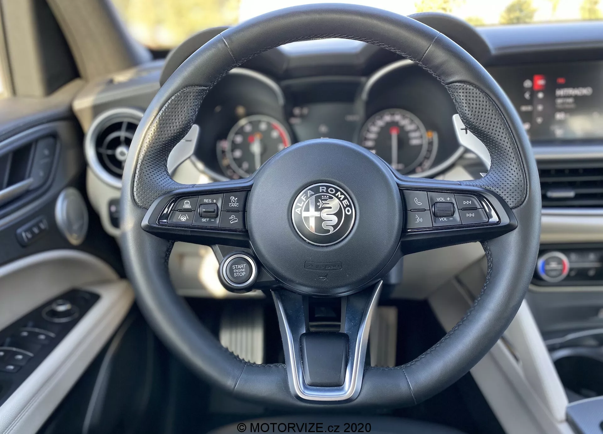 Vista en primer plano de la perspectiva del conductor desde el asiento del conductor en un vehículo Land Rover, destacando el moderno volante de tres radios con controles tecnológicos integrados y el sofisticado tablero con diales analógicos y una pantalla digital.