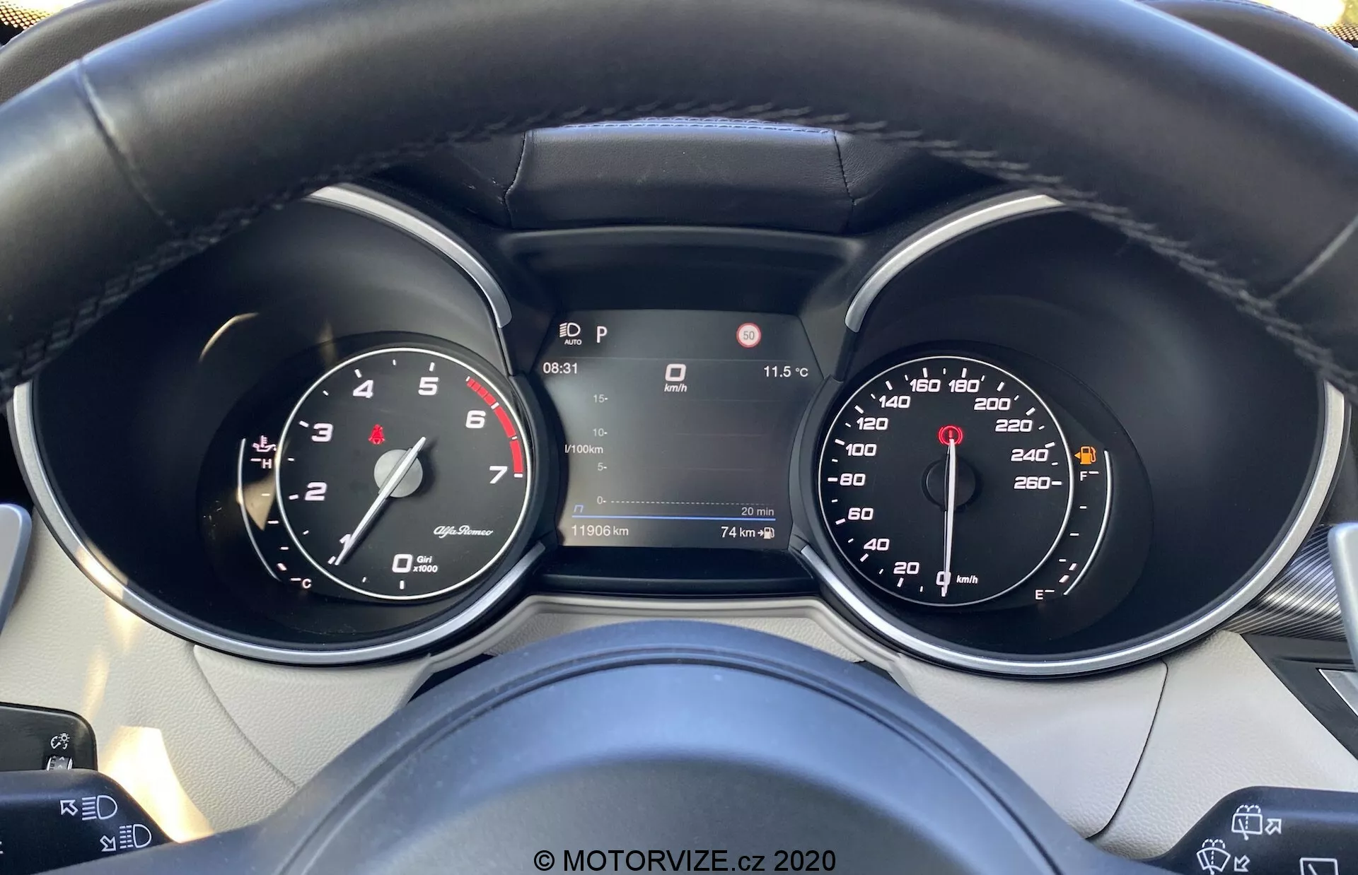 Vista detallada del panel de instrumentos del Alfa-Romeo Stelvio 2017 desde la perspectiva del conductor, mostrando el velocímetro, el tacómetro y una pantalla digital central en modo Park. El volante cuenta con botones de control, lo que sugiere comodidades tecnológicas avanzadas, y el panel incluye indicadores de temperatura, asistencia de mantenimiento de carril y otra información de conducción.