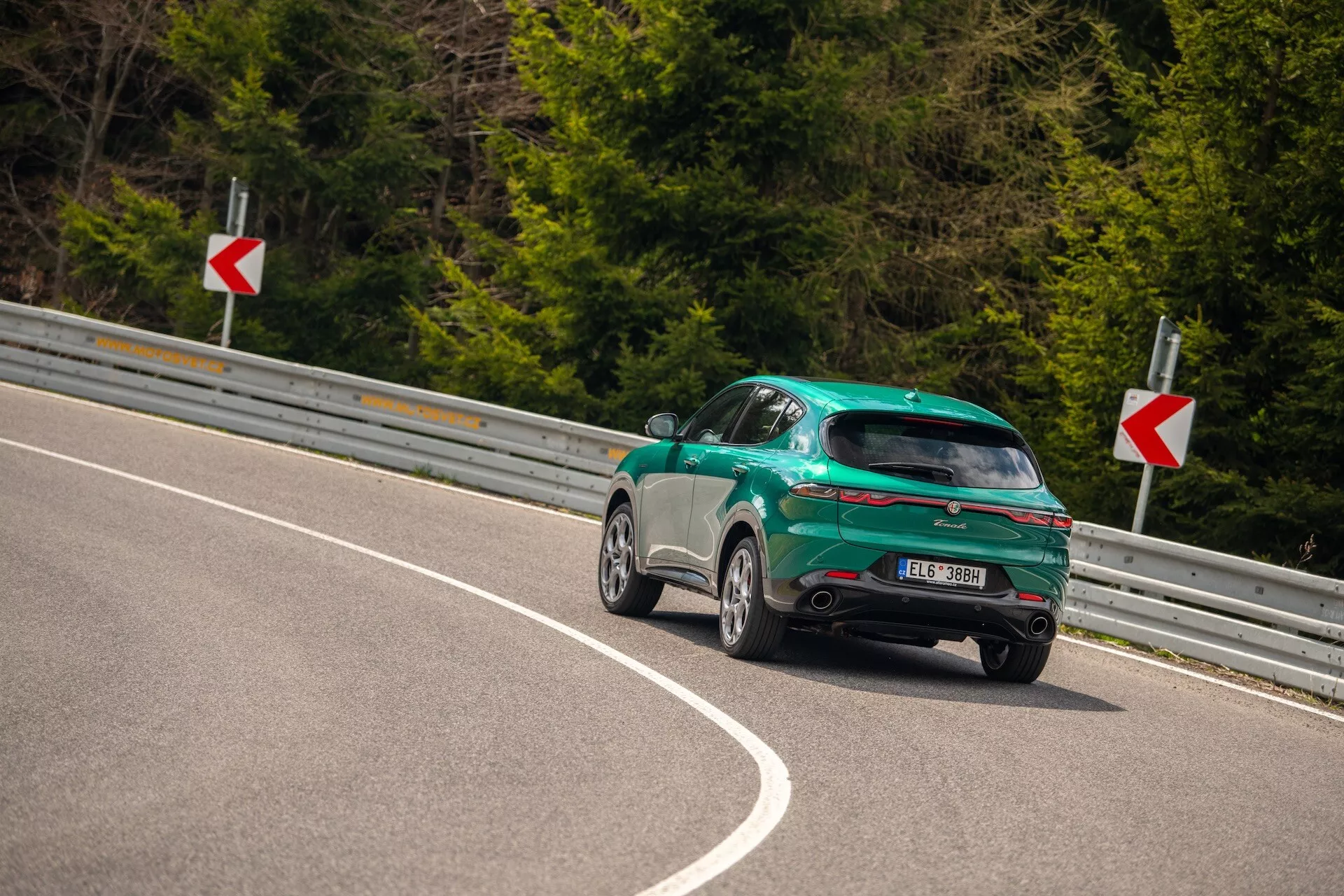 Alfa Romeo Tonale 2022 capturado desde un ángulo trasero de tres cuartos en una carretera curva, destacando su diseño deportivo tipo hatchback, acabado brillante y características aerodinámicas incluyendo un spoiler trasero, ruedas de aleación y luces traseras LED.