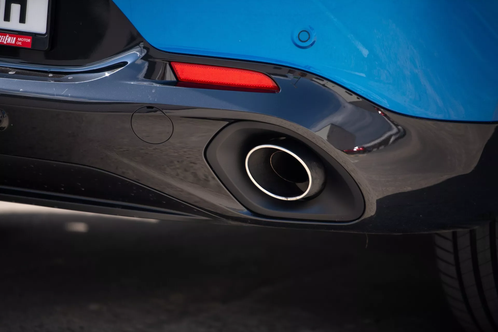 Primer plano de la sección trasera del Alfa Romeo Tonale 2022 destacando el tubo de escape deportivo, diseño aerodinámico del parachoques trasero y color azul de la carrocería con un atisbo de la luz trasera