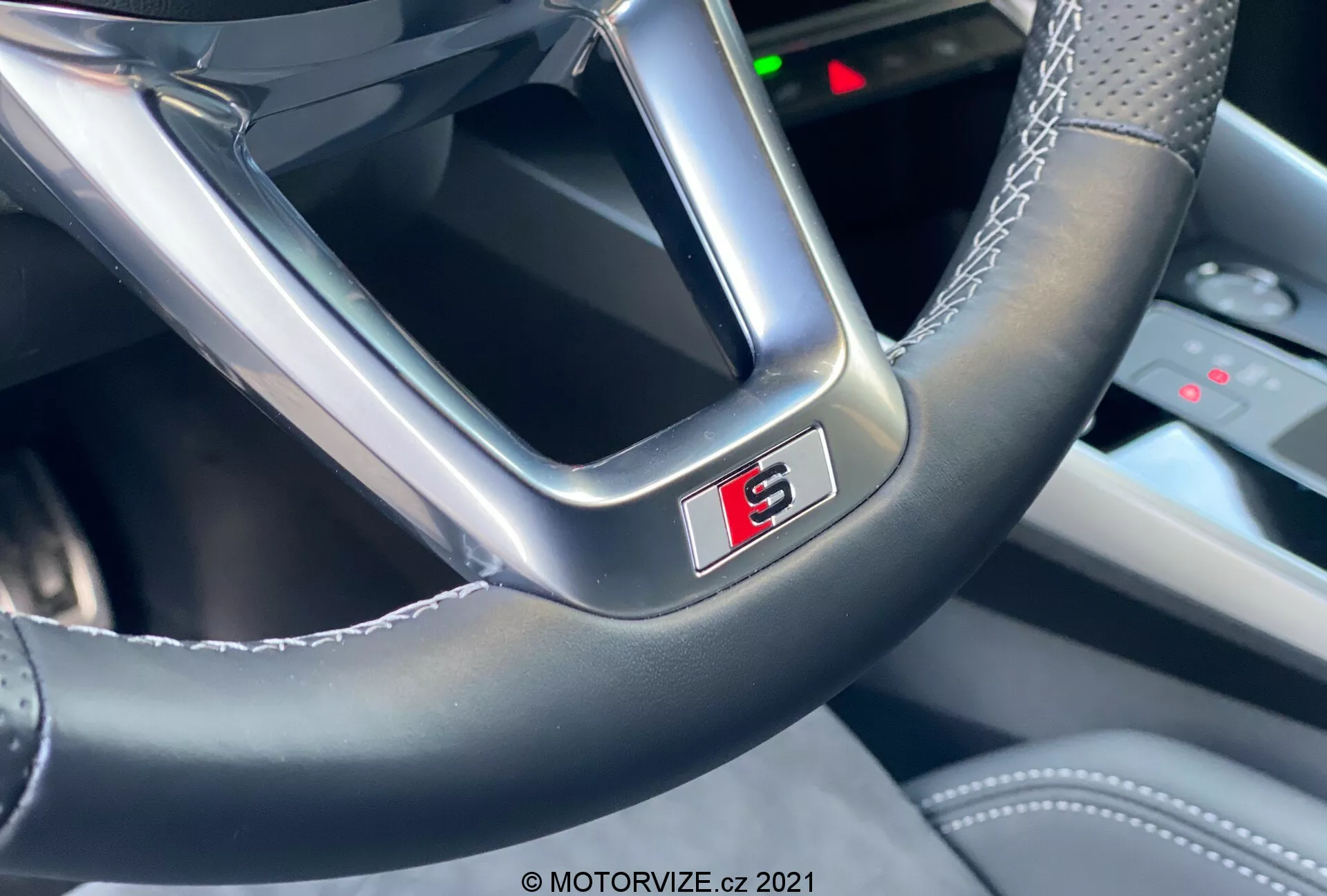 Vista de primer plano del volante de un coche moderno desde la perspectiva del conductor, centrada en la parte inferior que muestra una insignia 'S' prominentemente exhibida y bordeada en rojo. El volante muestra una combinación de cuero liso y material más brillante con costuras visibles, destacando la artesanía y el carácter deportivo del Audi A3 2020 Sportback.