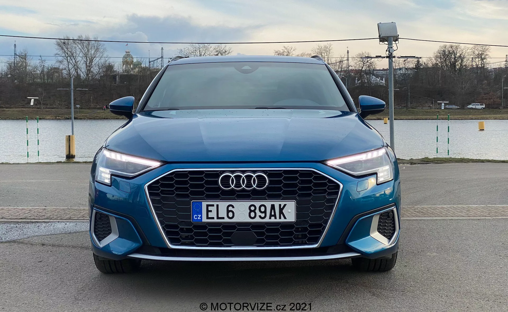 Vista frontal del Audi A3 Sportback 2020 azul que muestra su prominente parrilla Singleframe con diseño hexagonal, logotipo de Audi central, faros LED con luces diurnas y parachoques delantero con tomas de aire adicionales y posibles luces antiniebla, contra un fondo exterior.