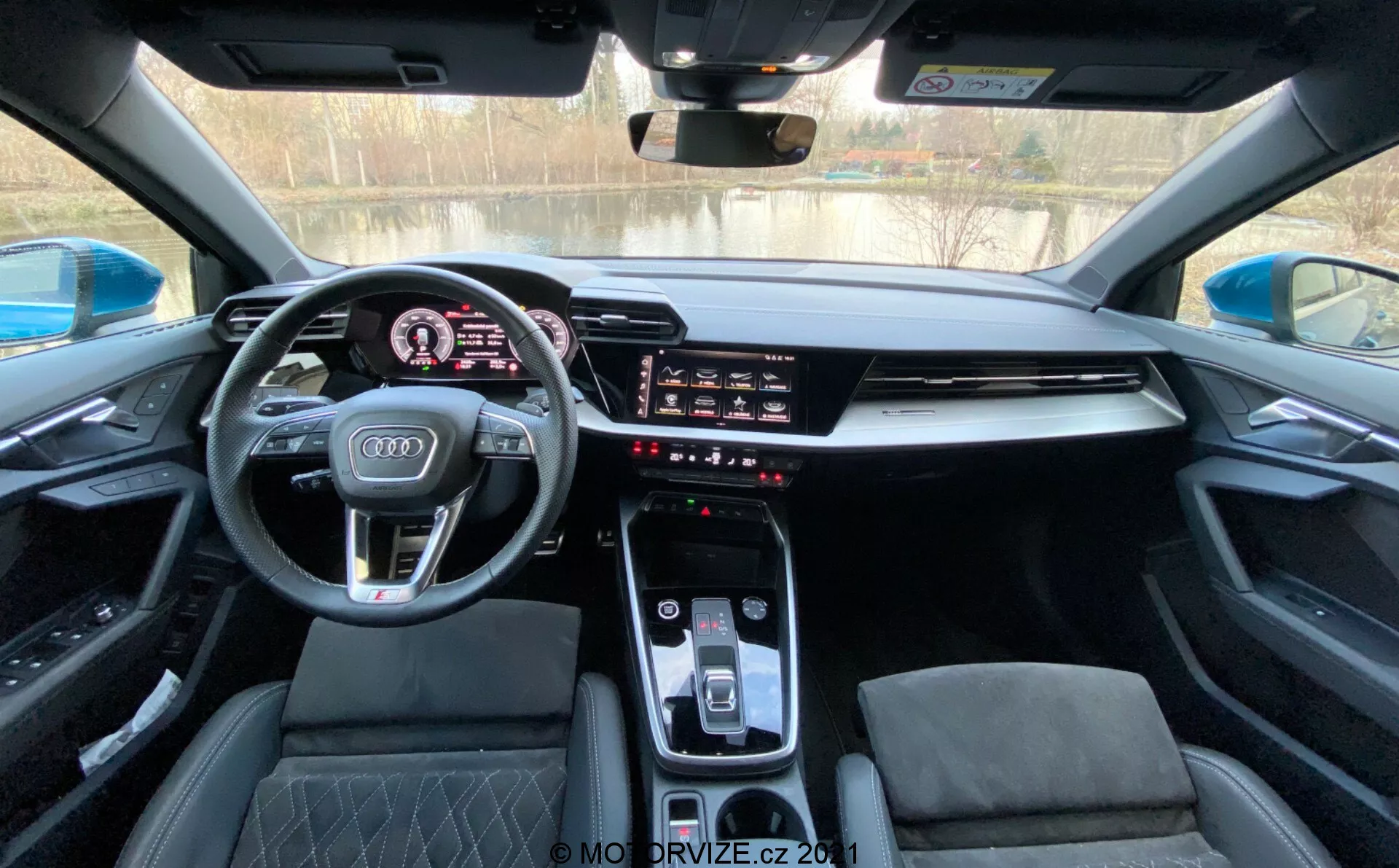 Interior del Audi A3 Sportback 2020 desde la perspectiva del conductor, mostrando un tablero moderno con un cuadro de instrumentos digital, volante deportivo multifuncional con el logo de Audi, pantalla táctil de infoentretenimiento integrada, consola central elegante con selector de cambios automático, controles de clima y asientos deportivos con acolchado de diamante bajo un techo solar panorámico.