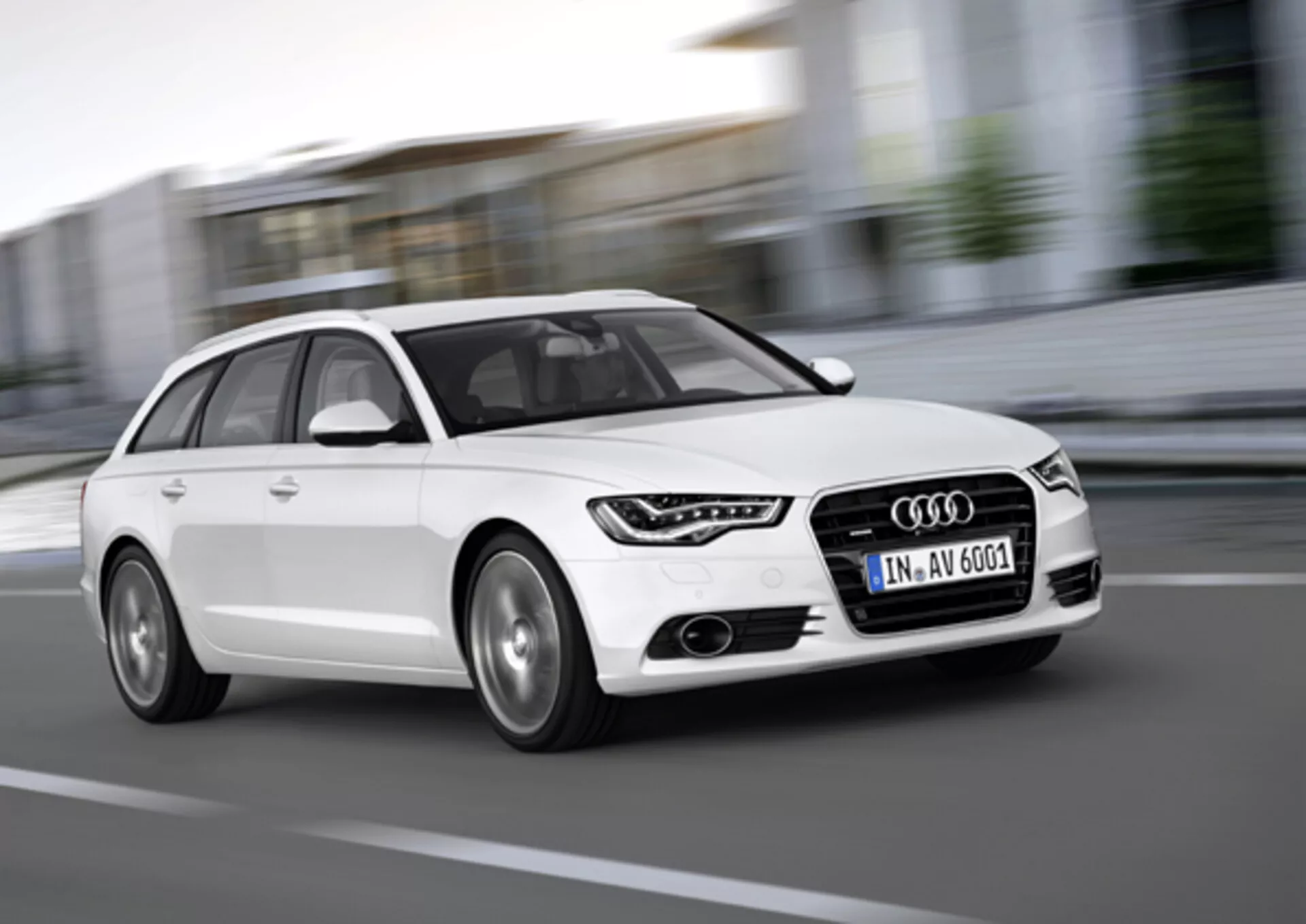 Audi A6 Avant blanco del 2011 en movimiento, capturado desde un ángulo bajo frontal de tres cuartos destacando la parrilla, luces diurnas LED, llantas de aleación y diseño dinámico