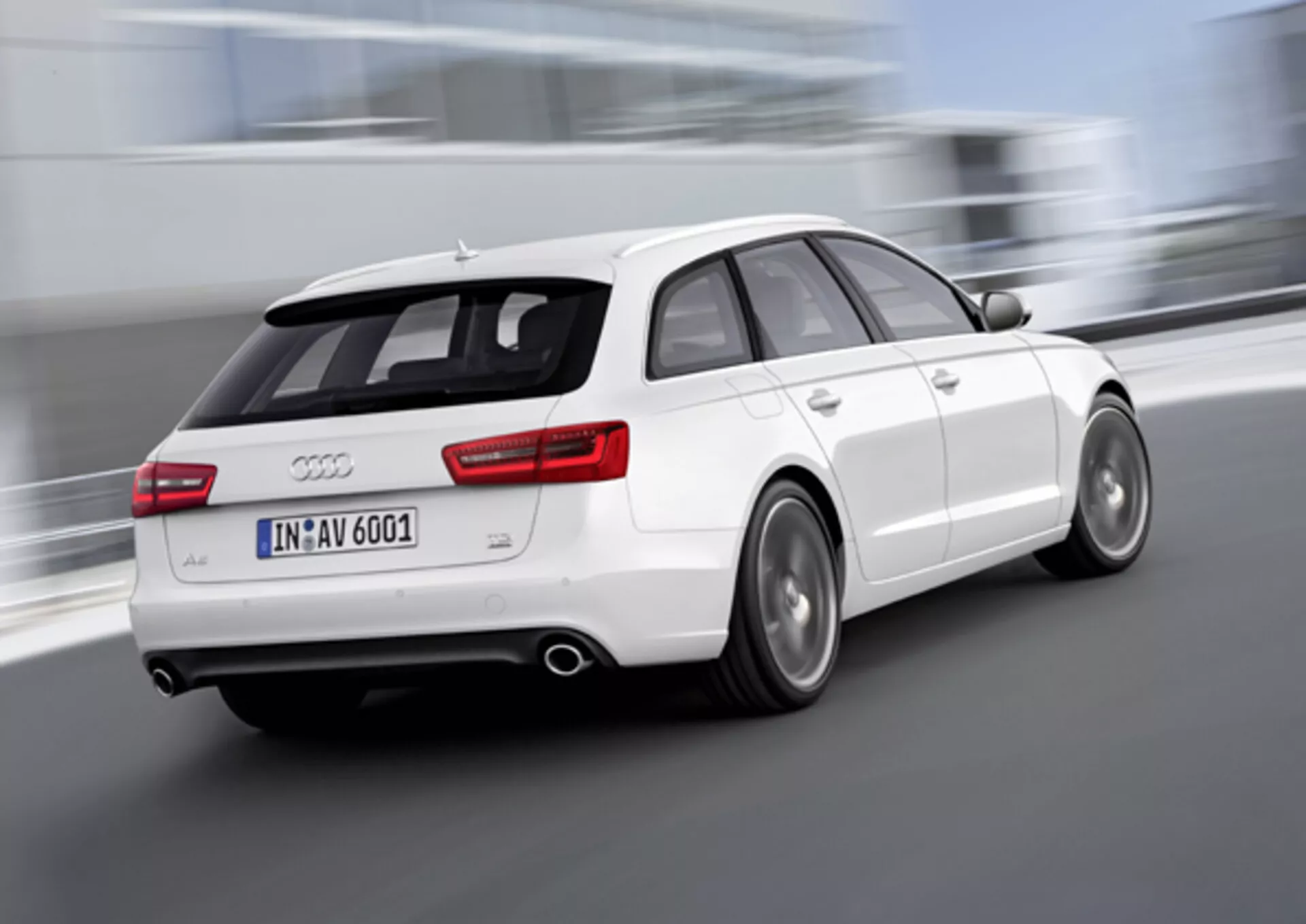 Vista trasera tres cuartos dinámica de un Audi A6 Avant blanco del 2011 en movimiento, con ruedas borrosas que indican velocidad, doble escape, llantas de aleación con frenos de disco visibles y spoiler montado en el techo para mejorar la aerodinámica, tomada al aire libre.