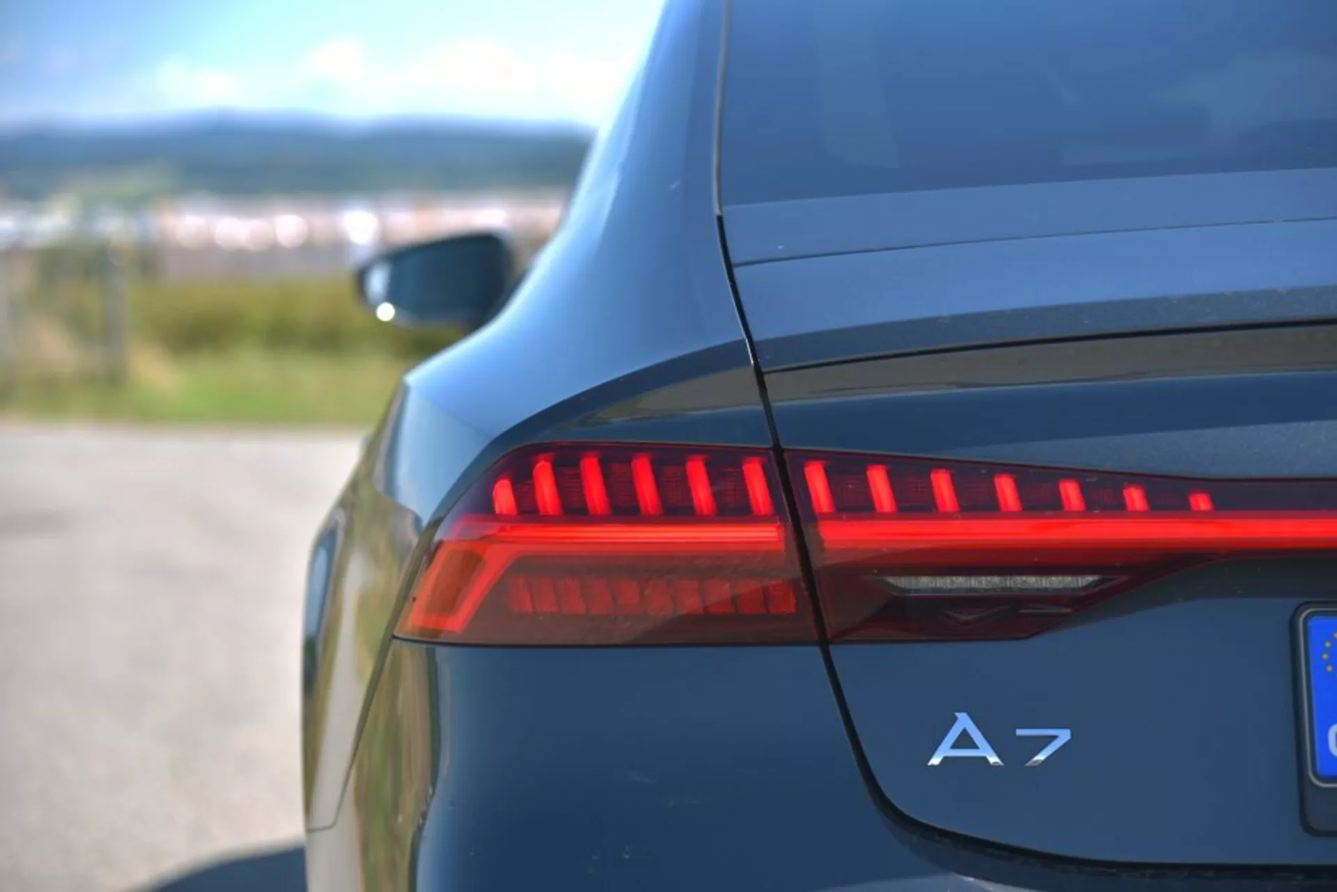 Vista detallada de la luz trasera LED iluminada y la insignia A7 en el lado trasero de un Audi A7 Sportback azul oscuro, destacando características de diseño automotriz moderno y detalles de lujo