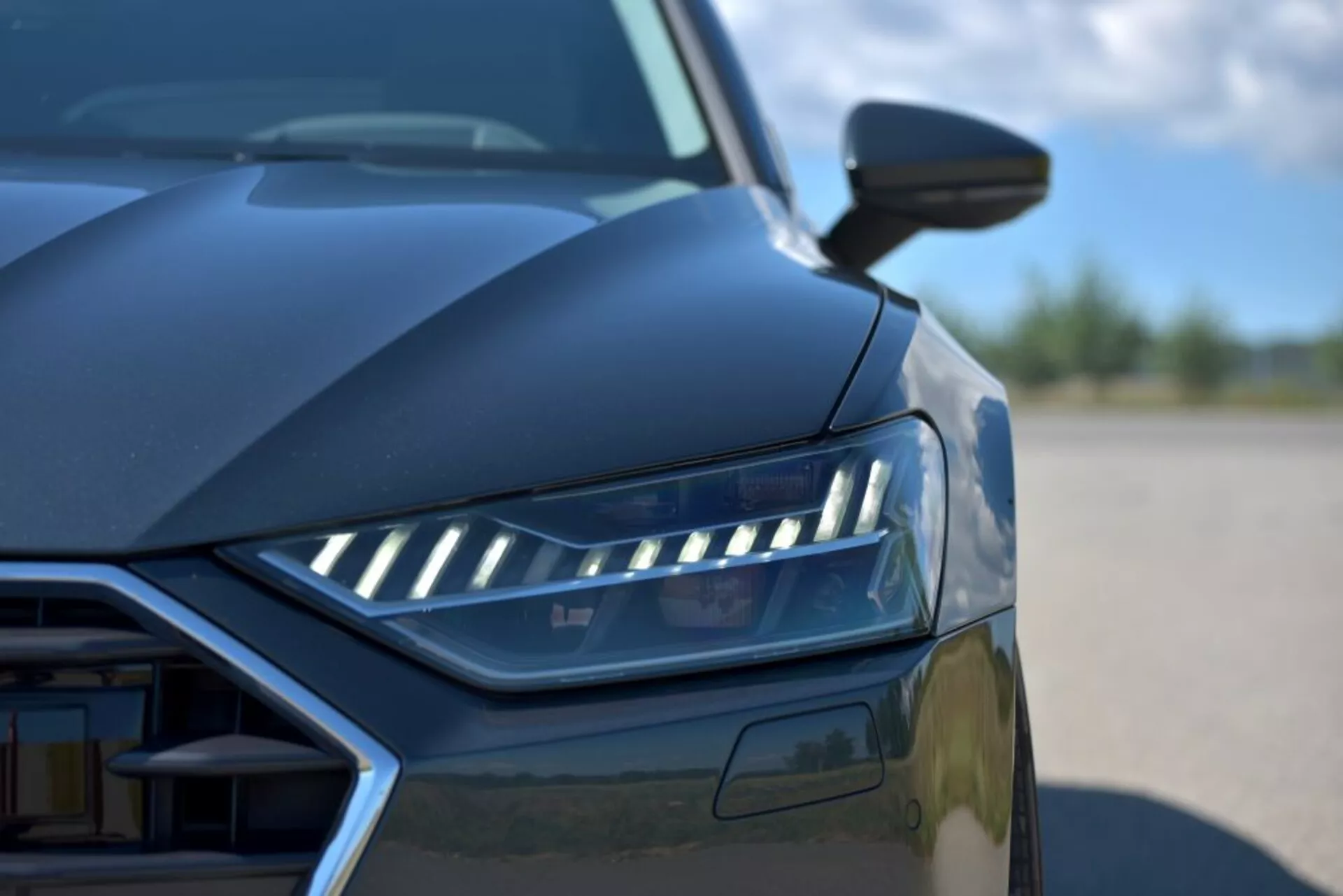 Primer plano del Audi A7 Sportback 2018 destacando el diseño de faros LED, vista parcial de la parrilla y líneas aerodinámicas desde un ángulo bajo, mostrando características de coche de lujo moderno y tecnología de iluminación avanzada