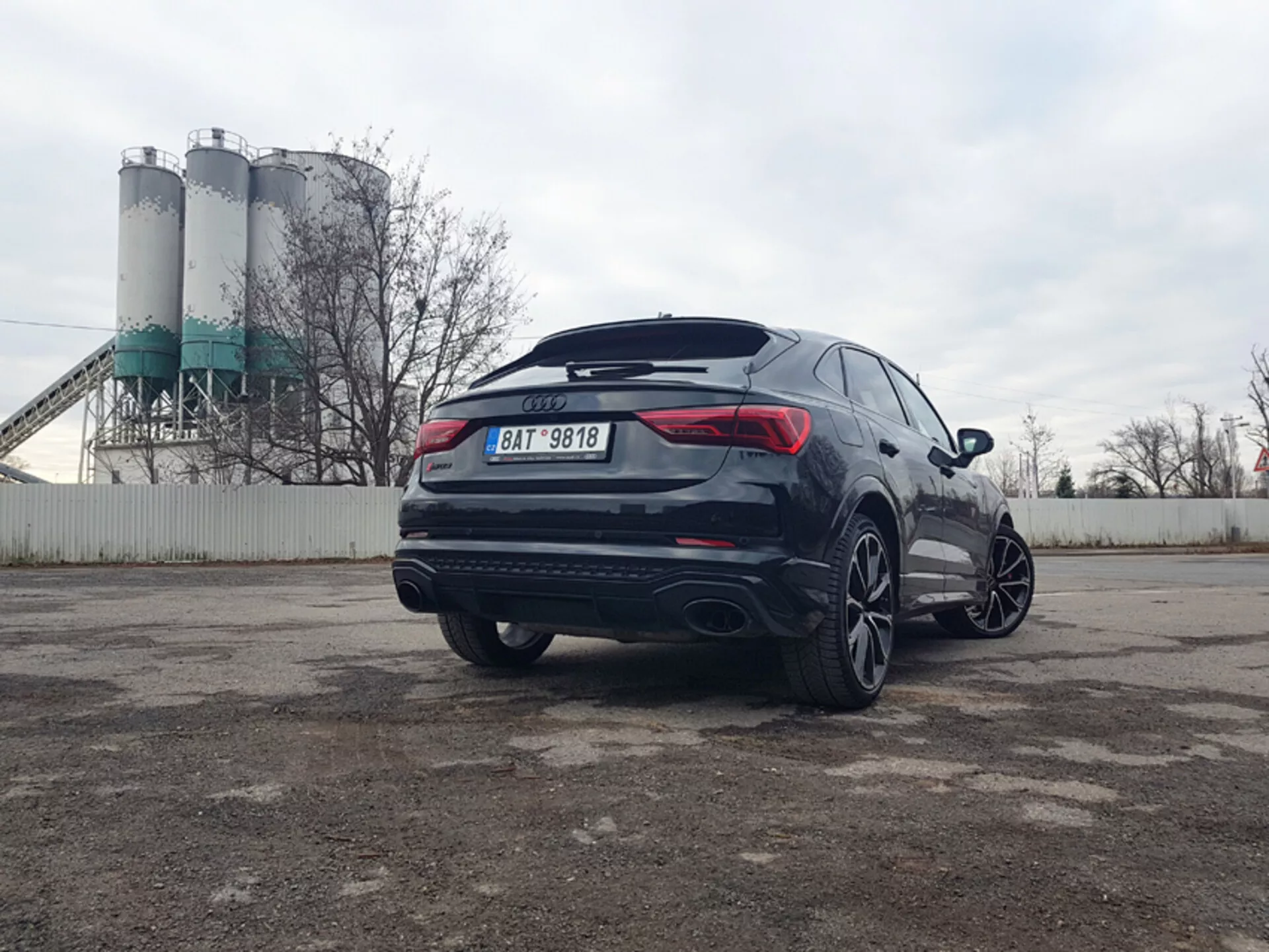 Audi Q3 RS del 2015, un SUV moderno con vista trasera de tres cuartos que muestra un diseño deportivo, grandes ruedas de aleación, sistema de escape doble y vidrios polarizados, estacionado en una zona industrial.
