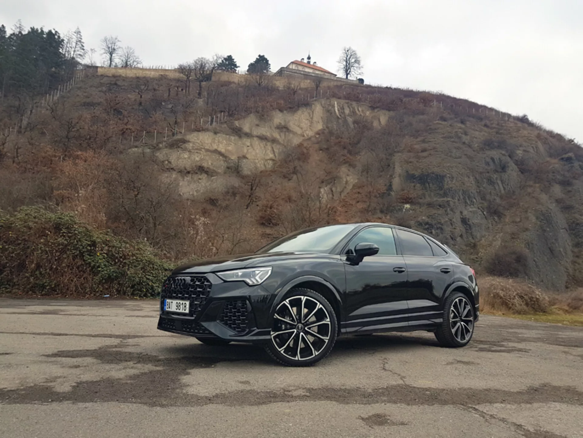 Vista lateral frontal del Audi RS-Q3 2015 aparcado al aire libre en un lote pavimentado con líneas desvanecidas, mostrando ruedas de aleación y parrilla frontal contra un telón de fondo de colina nublada