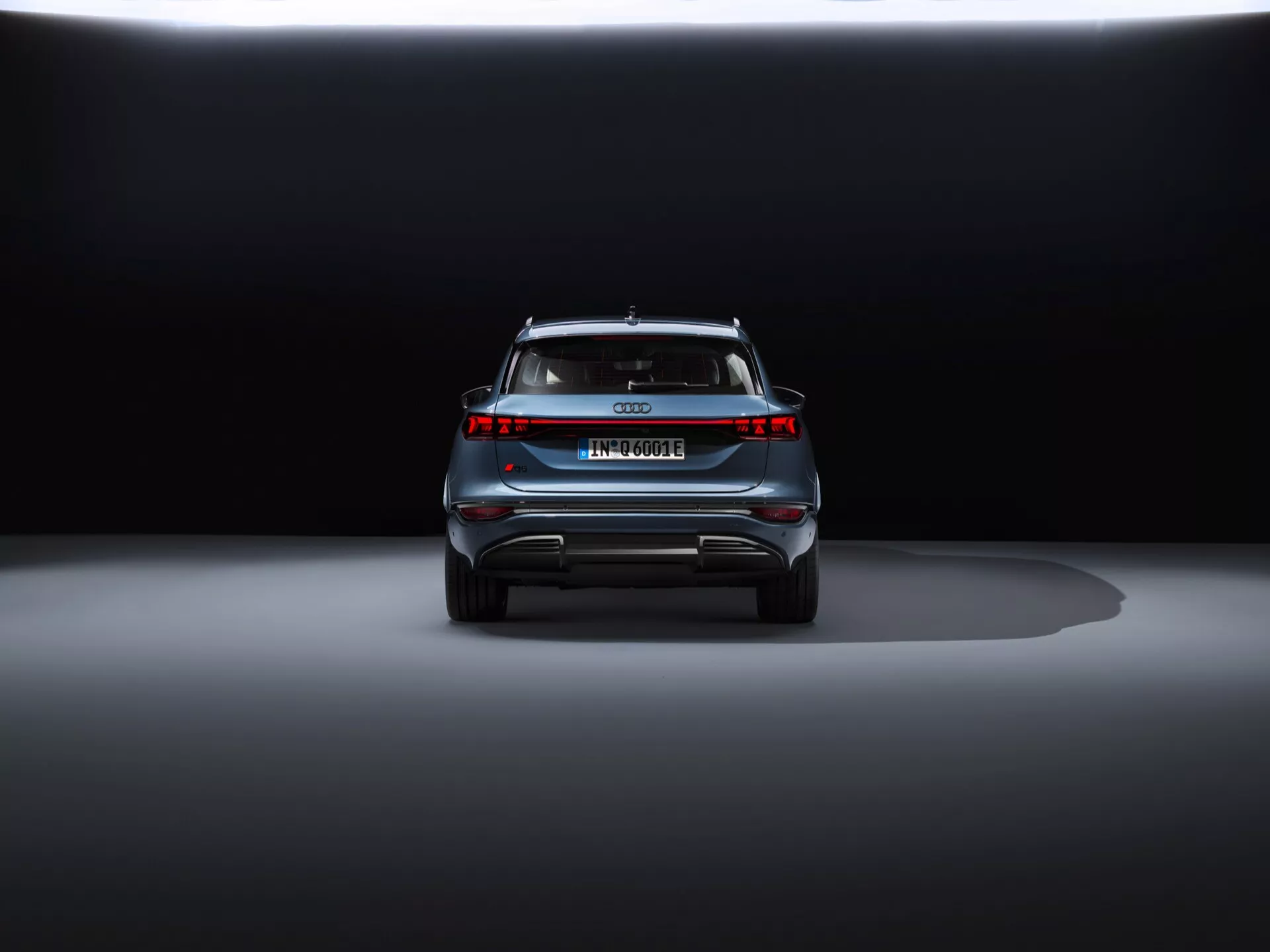 Vista trasera del Audi Q6 e-tron 2024 contra un fondo oscuro, mostrando su diseño elegante, emblema central, nombre del modelo, barra de luz horizontal, spoiler trasero y parachoques estilo difusor con elementos reflectantes.