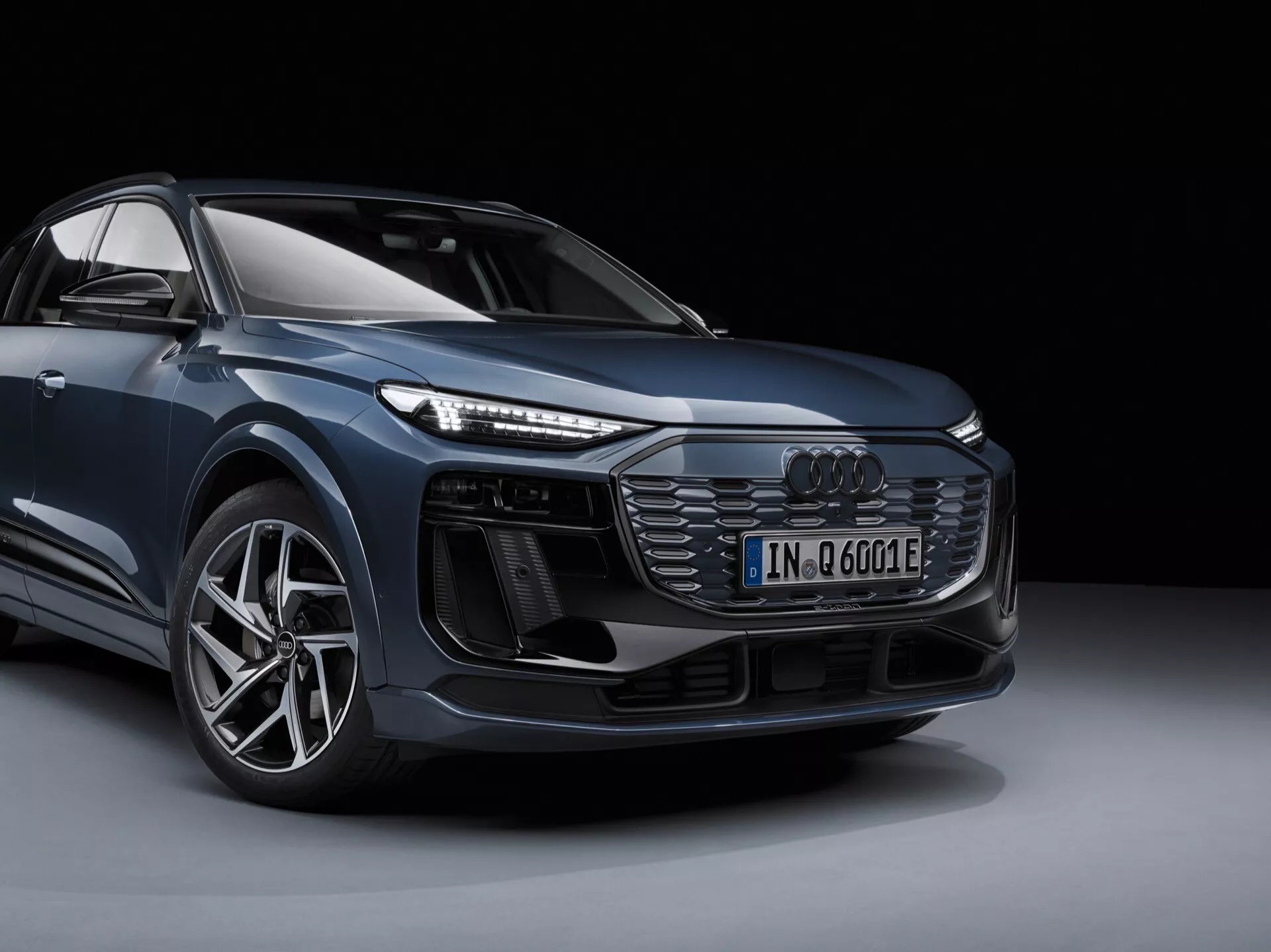 SUV de lujo Audi Q6 e-tron 2024 fotografiado desde un ángulo bajo de tres cuartos frontales, mostrando líneas elegantes del cuerpo metálico, grandes ruedas de aleación, faros LED distintivos y una parrilla frontal dominante contra un fondo oscuro.