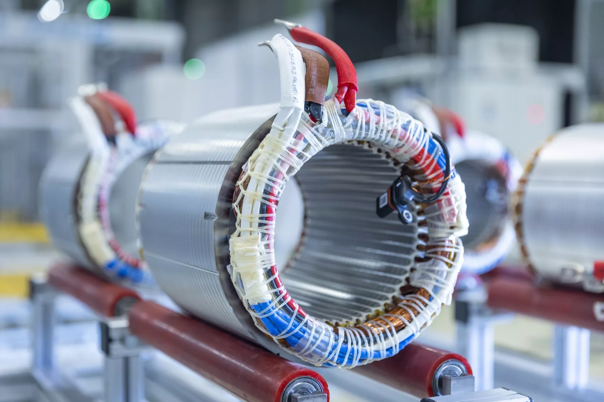 Foto de alta resolución de un estator de motor eléctrico montado en soporte rojo, mostrando bobinas de cable enrolladas alrededor de núcleos metálicos laminados típicos en maquinaria eléctrica para generar campos magnéticos