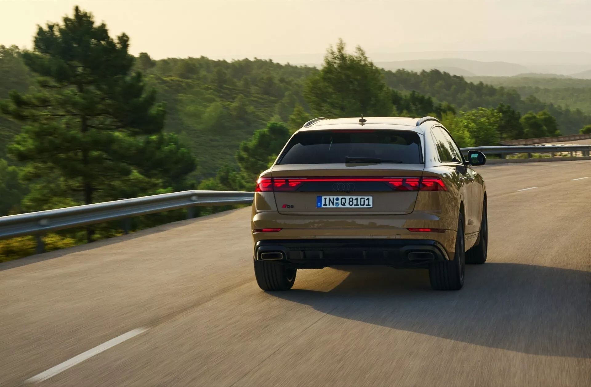Audi Q8 2023 (4M-Facelift) capturado desde una vista trasera de tres cuartos en movimiento, mostrando su diseño de luces traseras de ancho completo y puntas de escape dobles