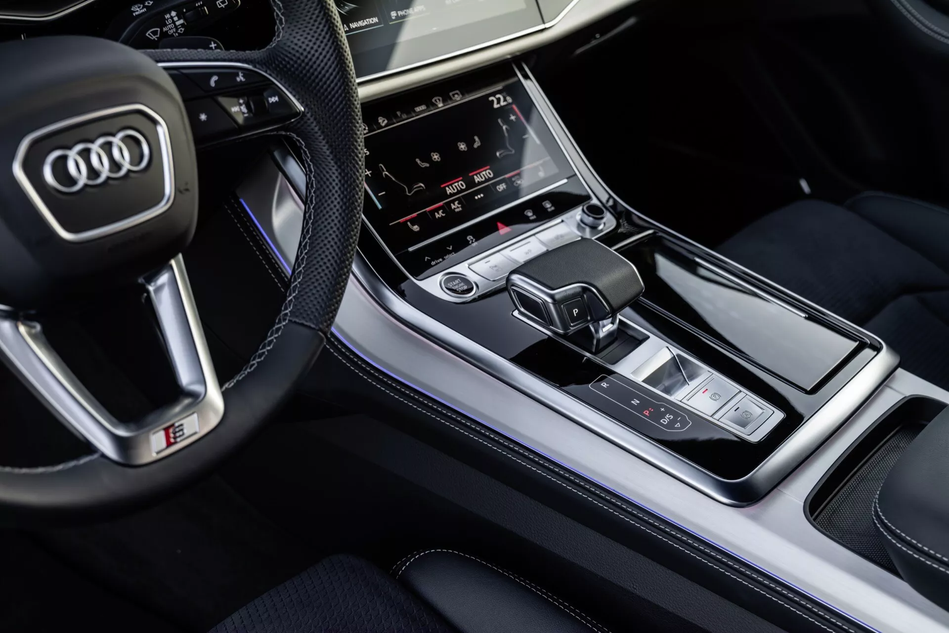 Vista aérea del interior de Audi Q8 2023 centrada en la consola central con el cambio de marchas y el panel de control multimedia, destacando acabados de lujo y características tecnológicas avanzadas