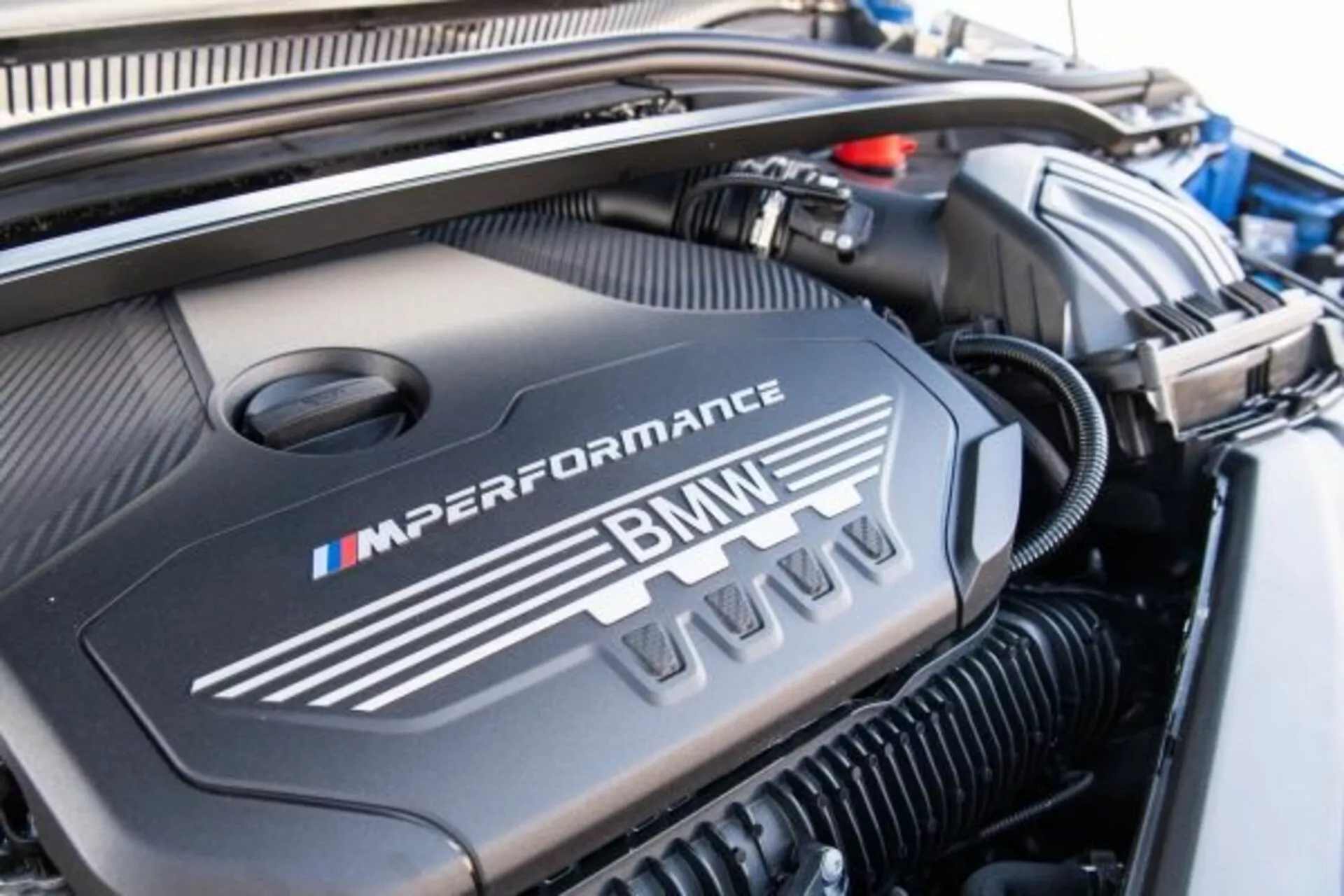 Imagen detallada del compartimento del motor de un BMW Serie 1 M Performance 2019, mostrando la cubierta del motor con el logotipo M en sus característicos colores azul, púrpura y rojo, destacando el diseño deportivo y de alto rendimiento.