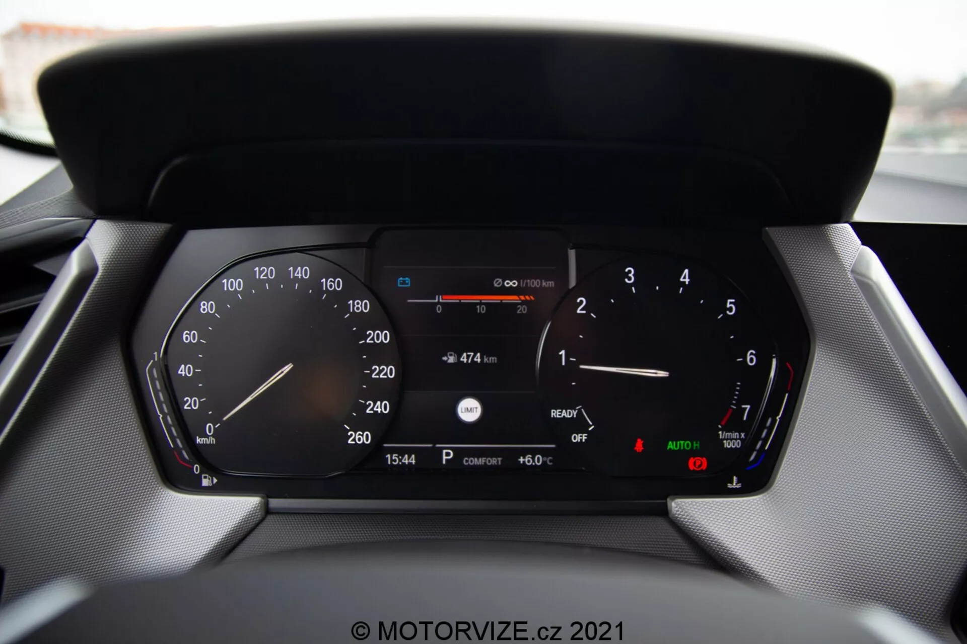 Vista de primer plano del cuadro de instrumentos digital de un coche moderno BMW Serie 1 2019 (BMW 116i), mostrando lecturas detalladas que incluyen velocímetro, tacómetro, indicador de combustible, medidor de temperatura, lectura digital de velocidad, distancia restante con el combustible actual, visualización del tiempo (15:54), temperatura externa (6.0°C) e indicadores para luces automáticas y freno de mano.