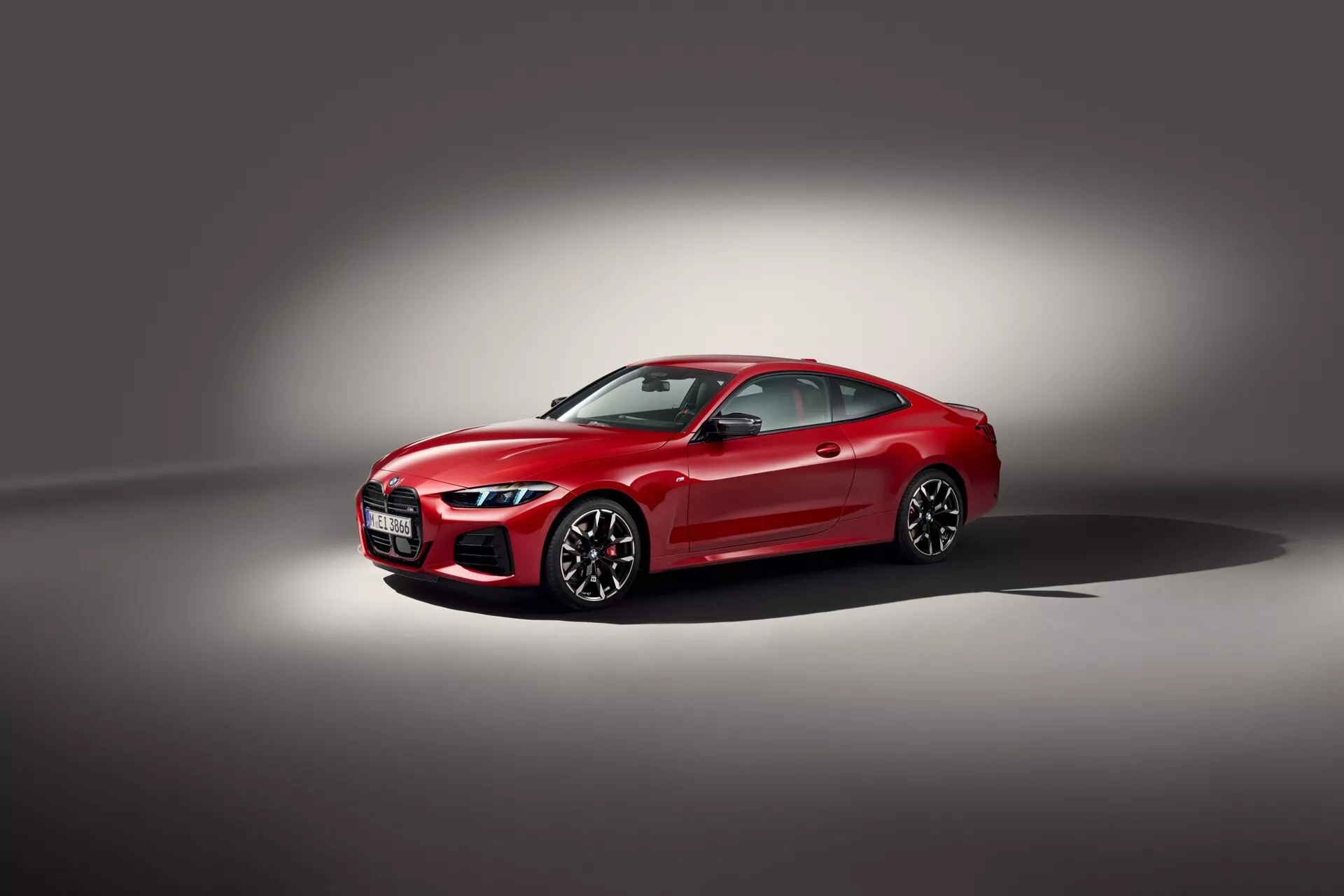 Coupé BMW Serie 4 2024 (G22-G23-G26-G82-G83 Facelift) en rojo, mostrando su parrilla frontal deportiva con emblema, faros delanteros LED angulares estrechos, espejos laterales aerodinámicos, ventanas tintadas, ruedas de aleación de múltiples radios con frenos de alto rendimiento, en un entorno de estudio con focos que resaltan sus características de lujo y tecnología avanzada