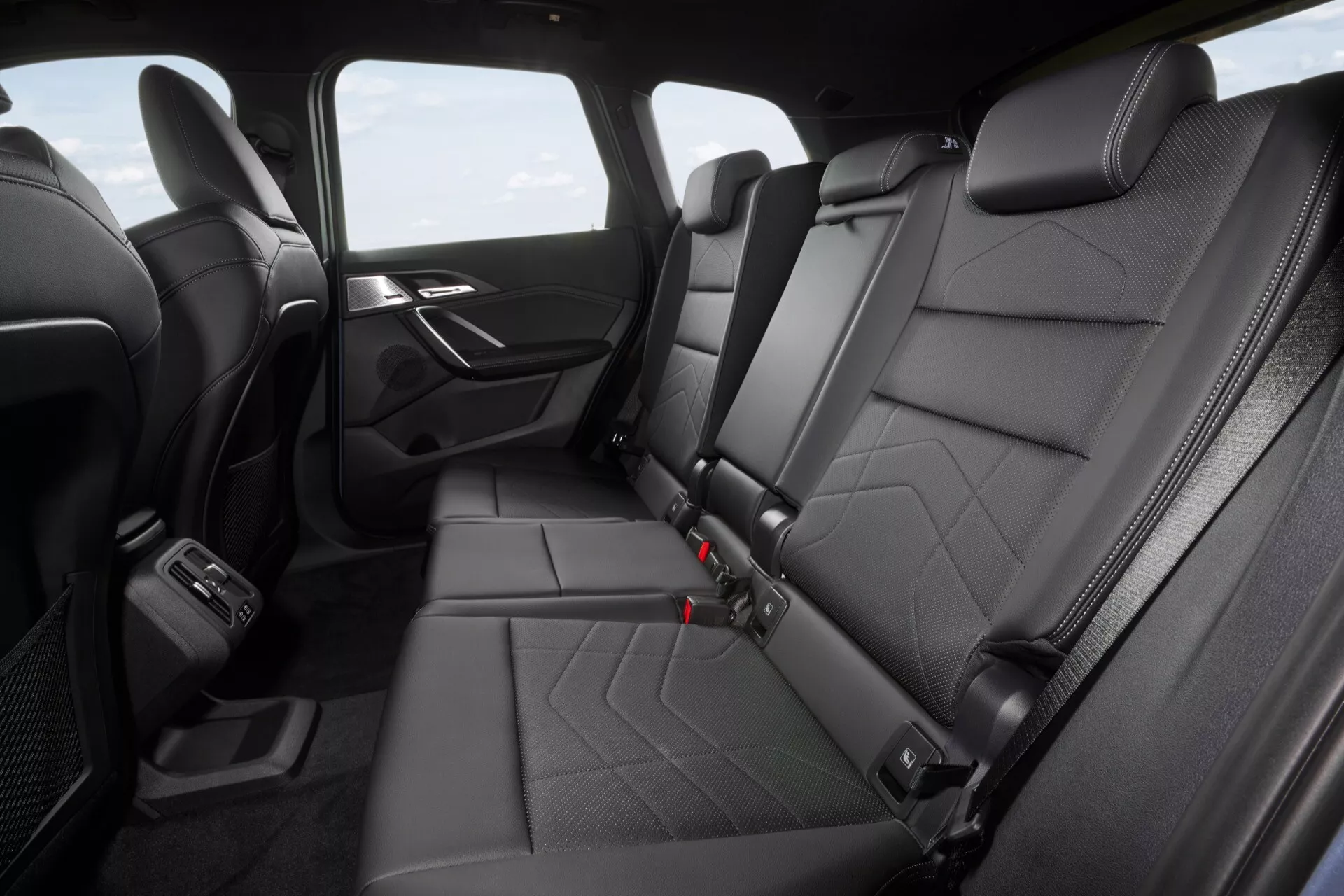Vista interior del compartimento trasero de un BMW X1 (U11) 2022 que muestra asientos de cuero acolchado, apoyabrazos integrado, panel de puerta con altavoz y control, cinturones de seguridad y respiraderos de control climático