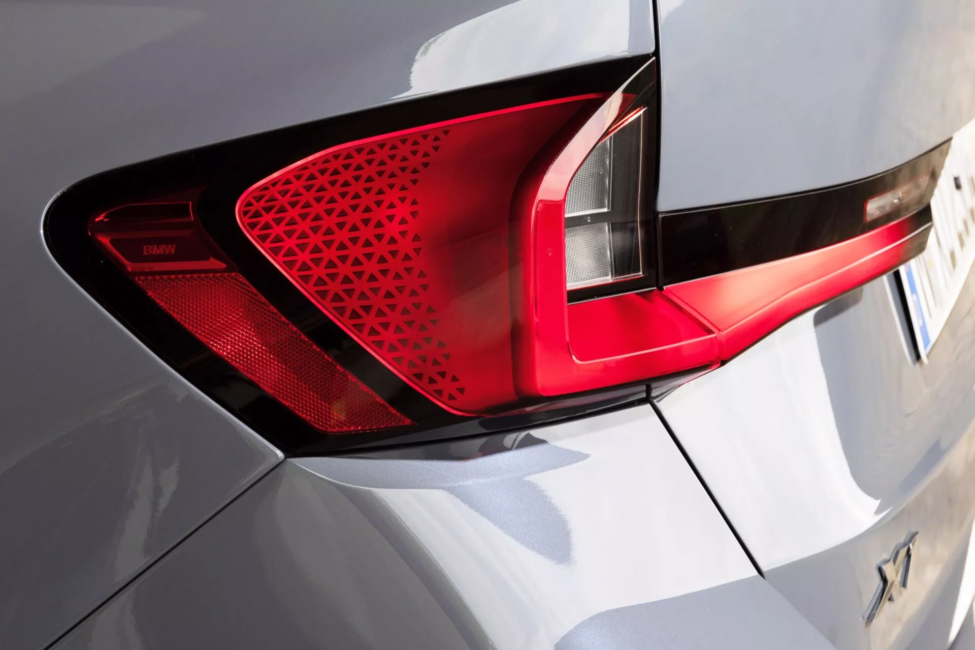 Vista lateral trasera detallada del BMW X1 (U11) 2022 enfocando el conjunto de luces traseras LED con patrón detallado de panal, carrocería brillante en plata o blanco destacando características de diseño aerodinámico moderno
