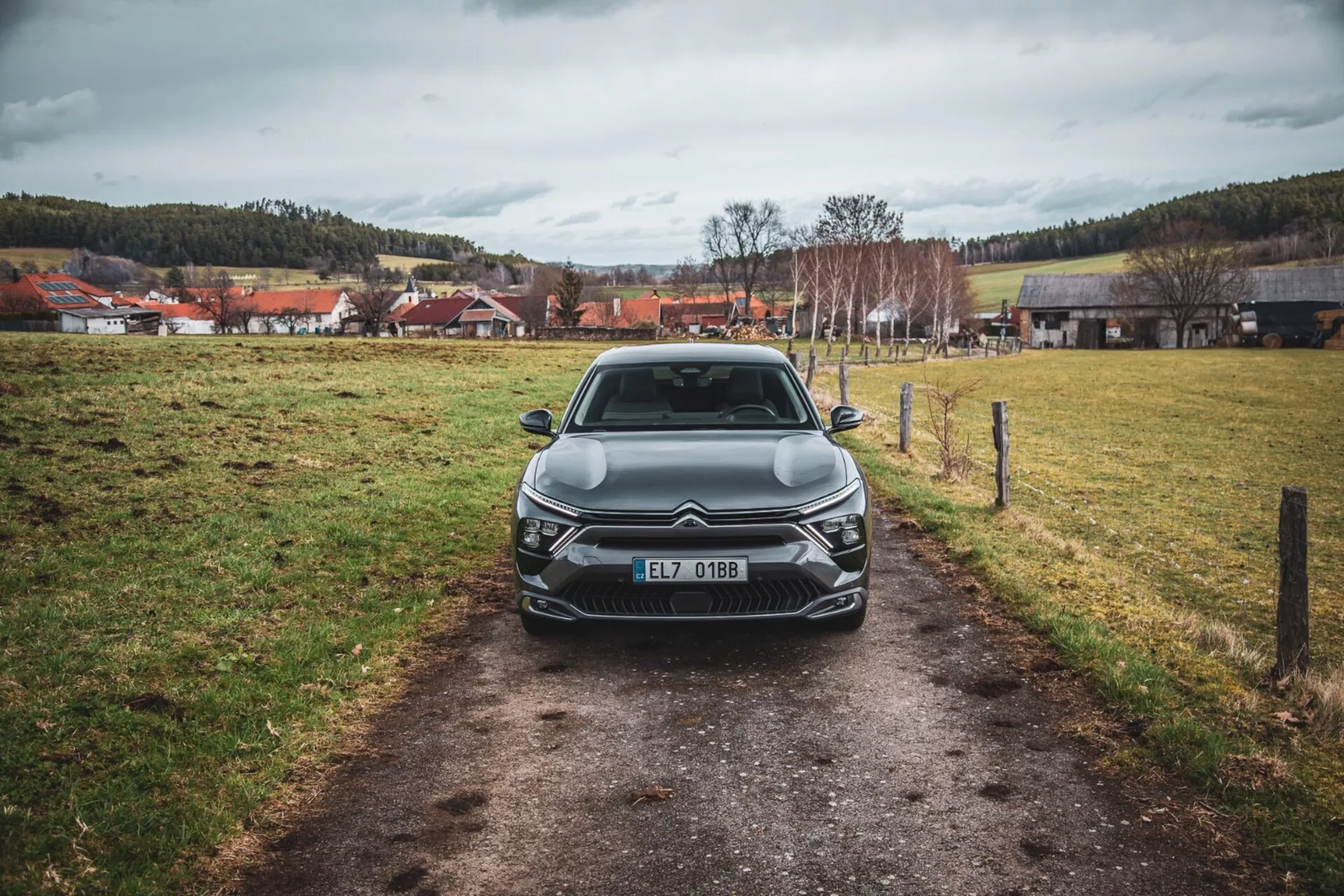 Vista frontal de un Citroën C5-X 2022 en un angosto camino en un campo de hierba bajo un cielo nublado, mostrando su elegante diseño, parrilla intrincada con emblema, unidades de faros LED angulares, líneas esculpidas en el capó y elementos adicionales de iluminación frontal, registrado en la República Checa.