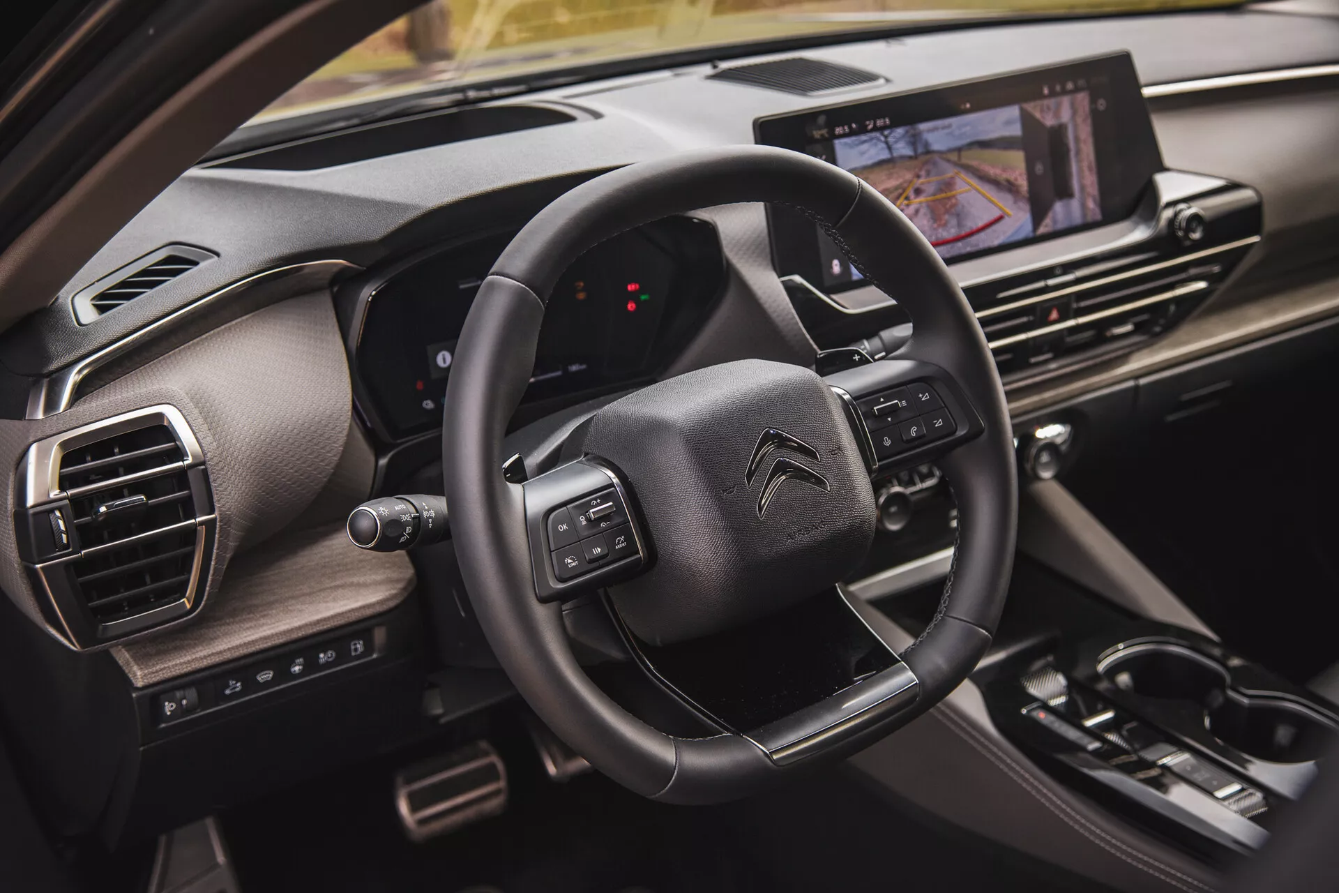 Vista cercana del interior del Citroën C5-X 2022 mostrando el volante con botones multifunción, un panel de instrumentos digital desde la perspectiva del pasajero y un sistema de infoentretenimiento con pantalla táctil